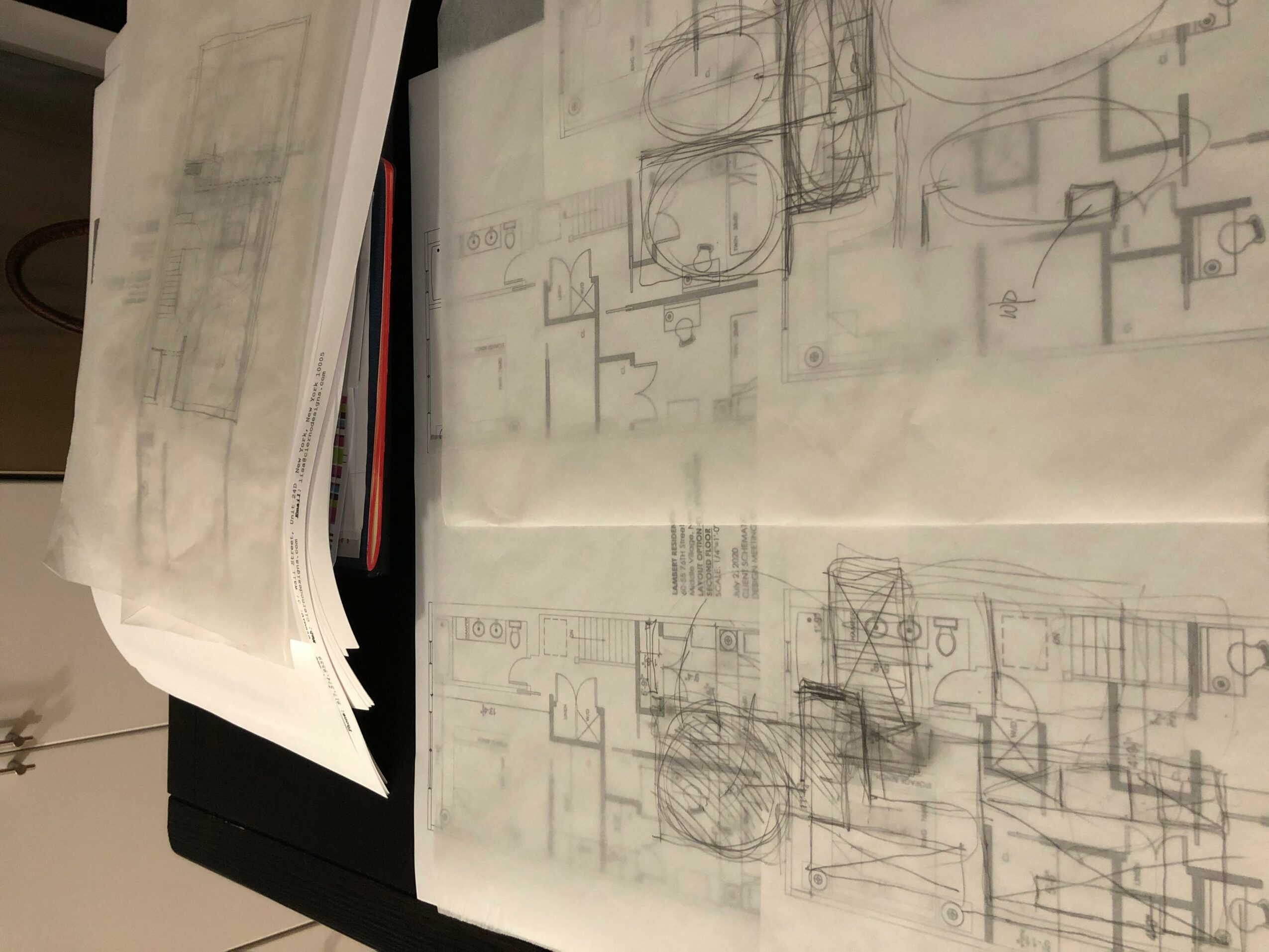 Architectural sketches and plans on paper, with some overlapping, on a dark surface.