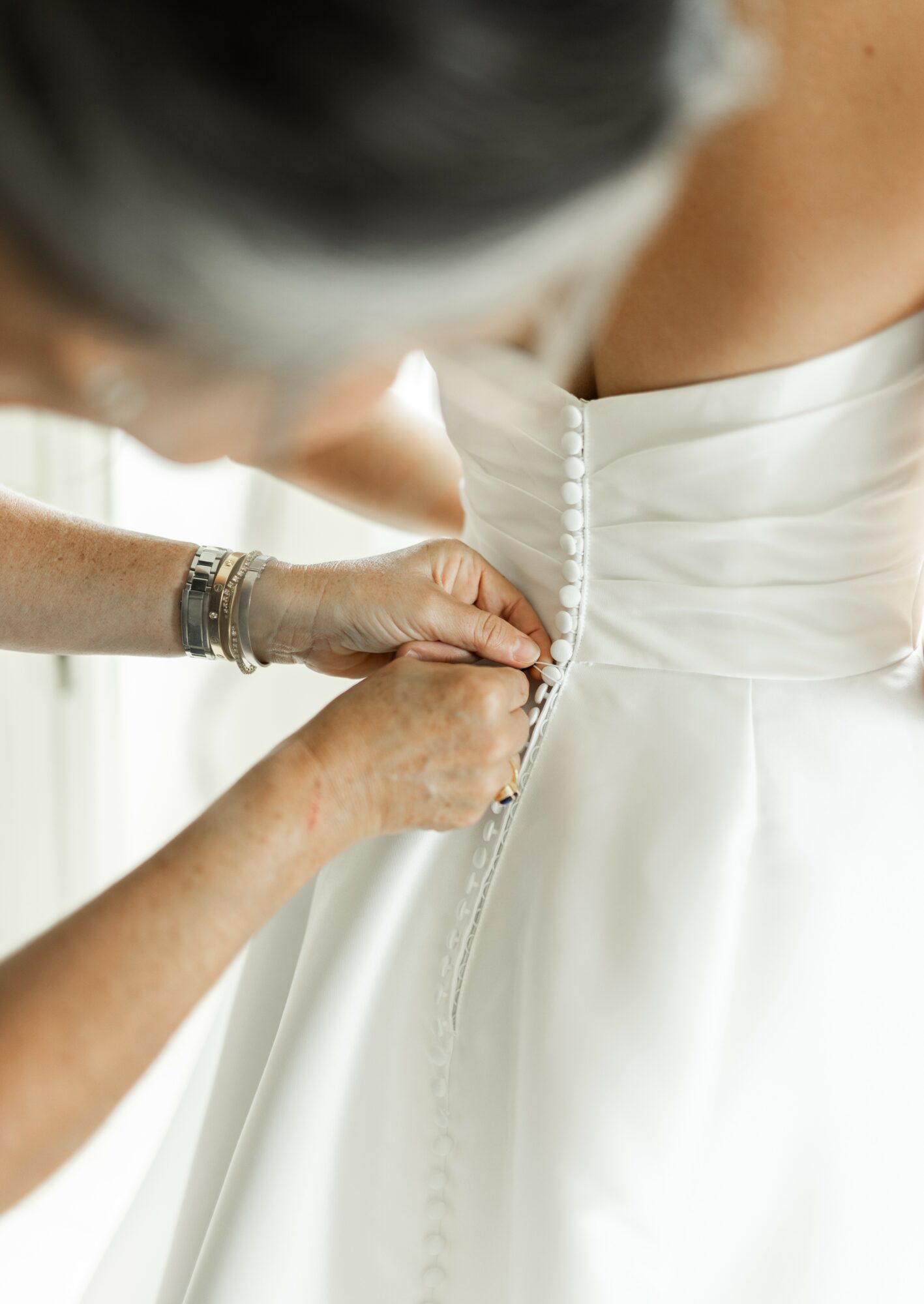 Person adjusting a white wedding dress zipper, focusing on hands and dress fabric, with blurred background.