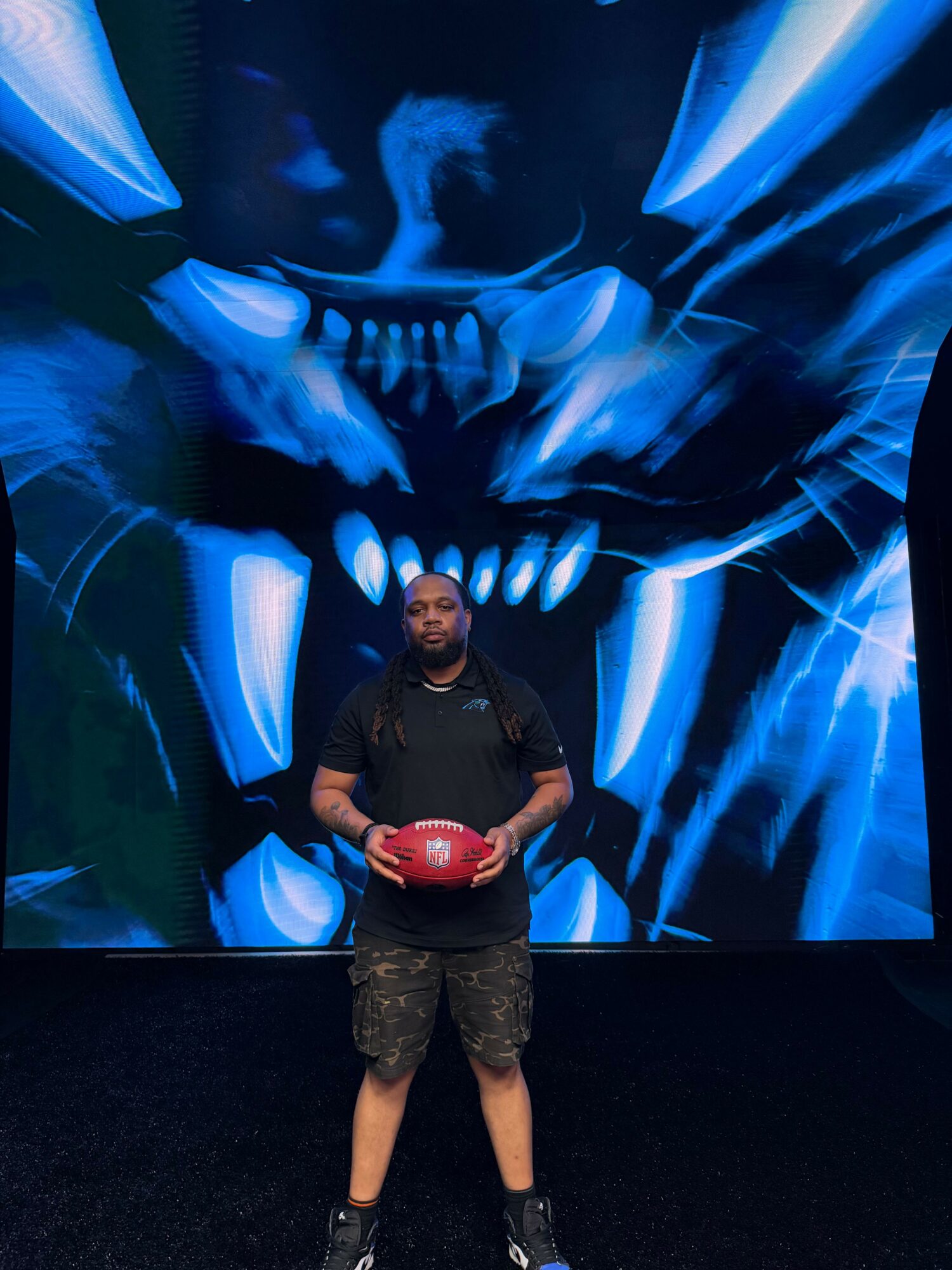 Person holding a red ball in front of a blue abstract background, standing sideways with one hand on hip.