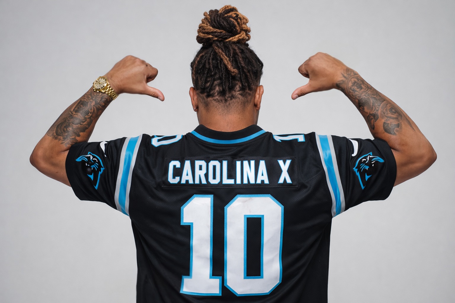 Person with braided hair and tattoos flexing arms, wearing a black sports jersey with Carolina X and number 10, facing away.