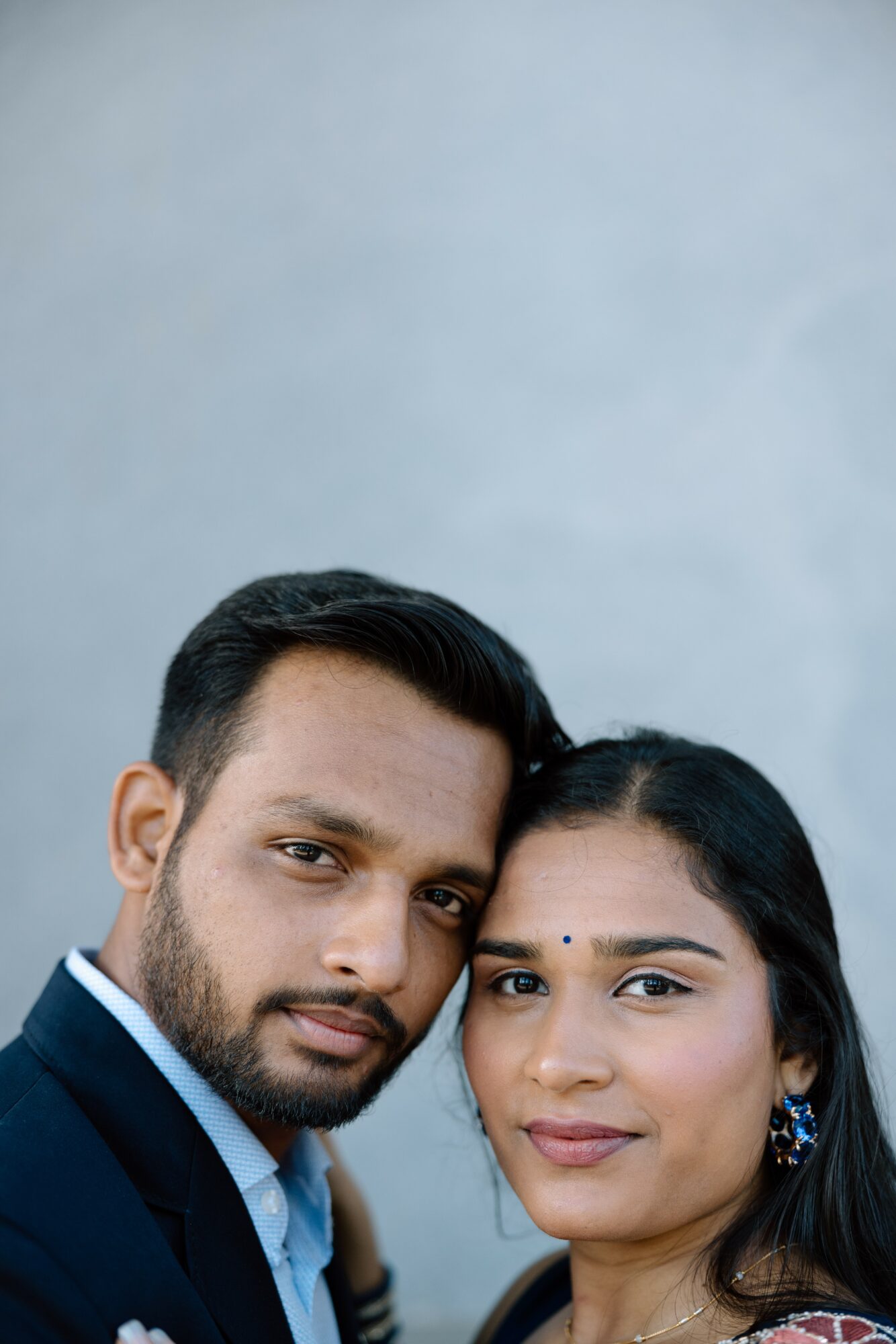 Close-up of a man and woman with dark hair and eyes, smiling, against a plain light background.