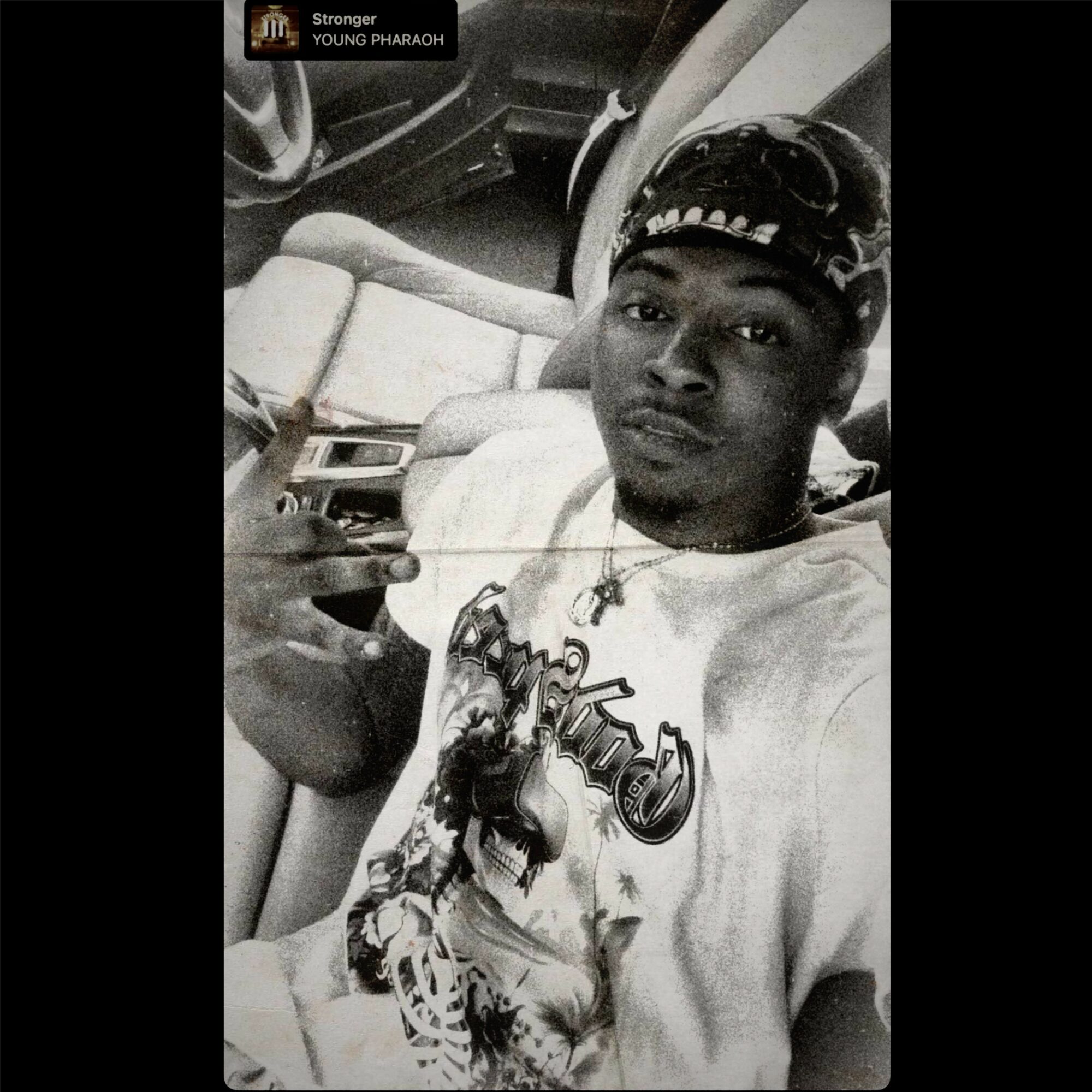 Young man taking a selfie in a car, wearing a cap and graphic t-shirt, holding a phone, with a serious expression.