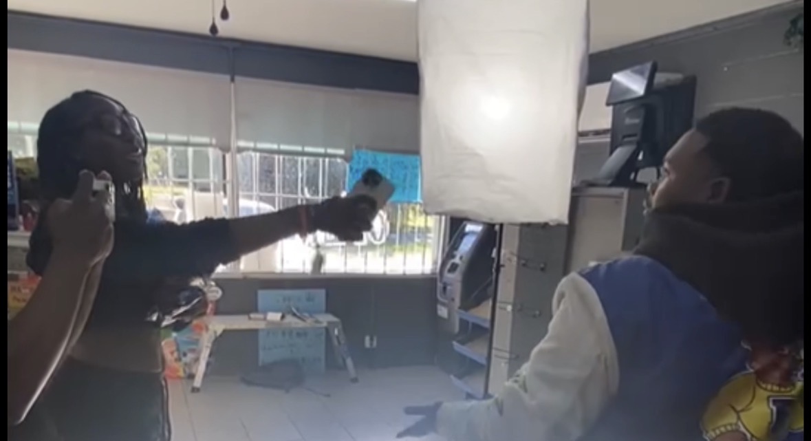 Person holding a spray bottle inside a room with a window and a person facing away, wearing a jacket.