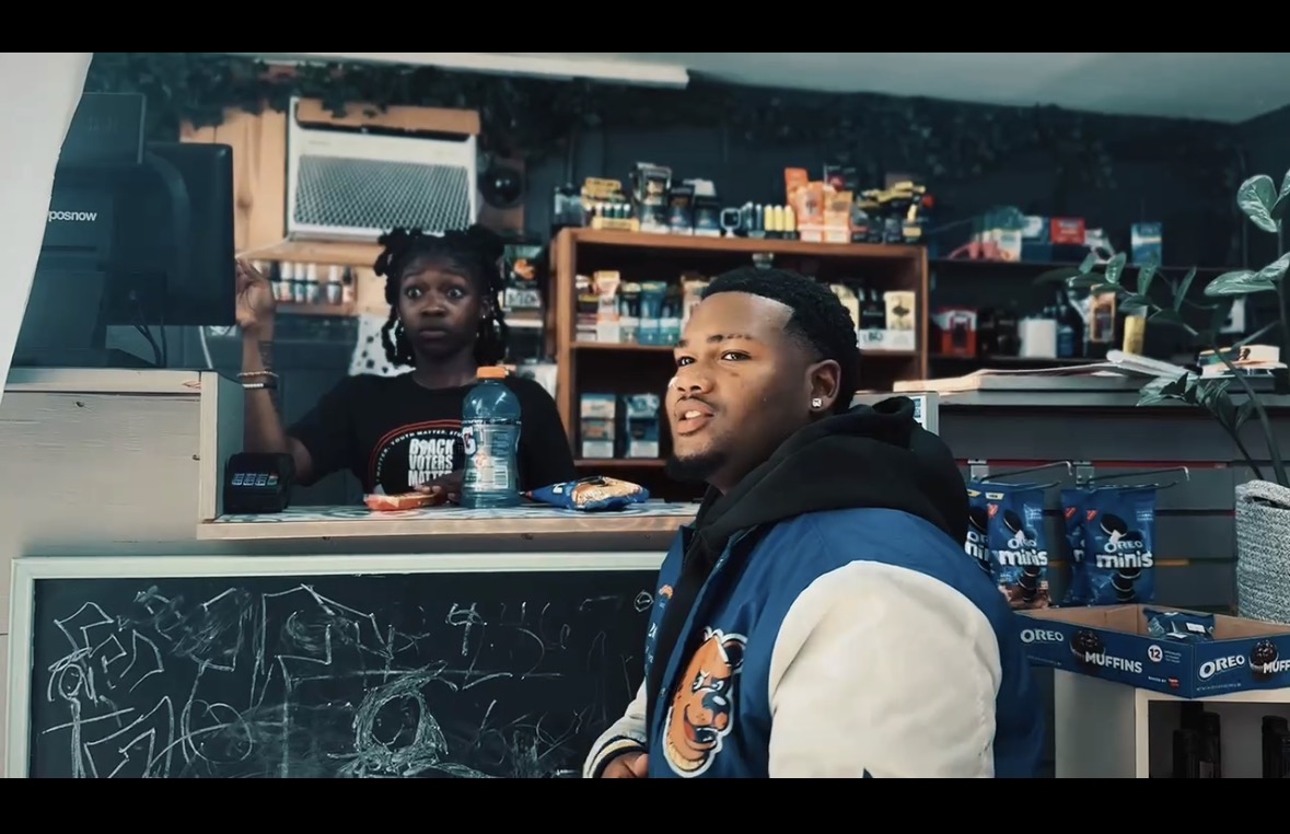 Two young people in a store or cafe with shelves of products behind them, one smiling and the other looking at the camera.