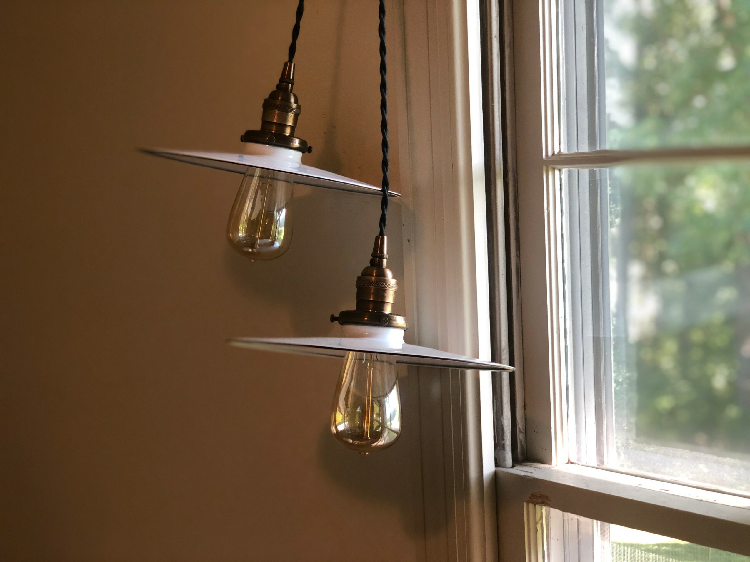 Two hanging pendant lights with exposed bulbs near a window, with a view of trees outside.