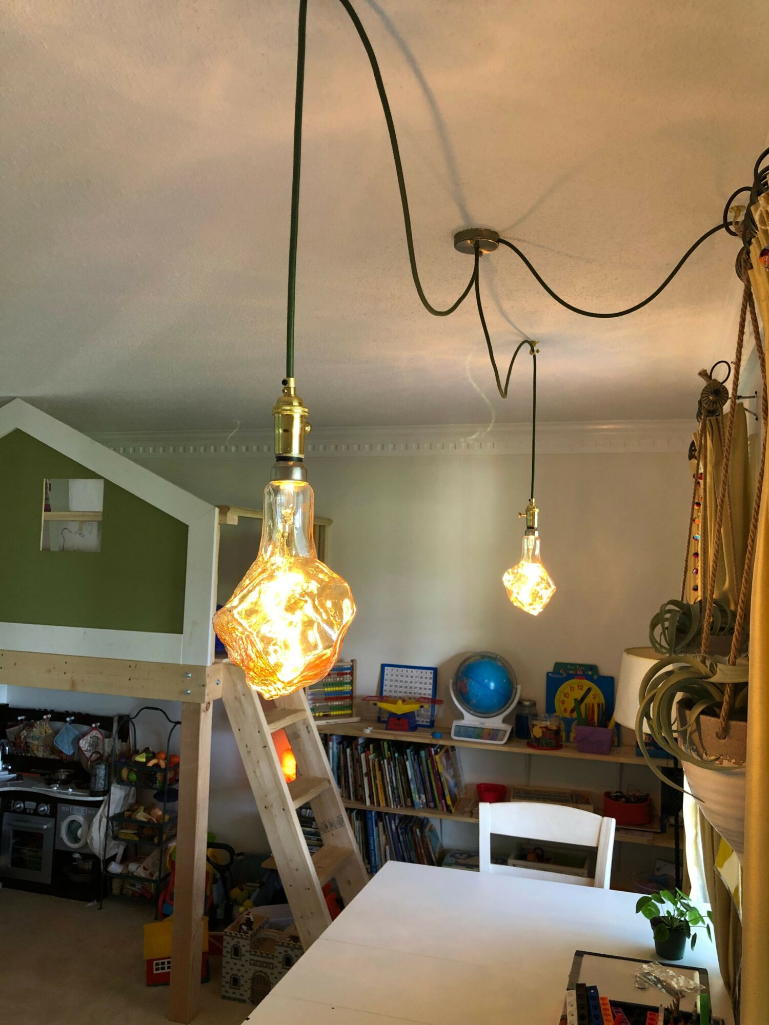 Two hanging light bulbs, one glowing brightly, in a room with shelves and books in the background.