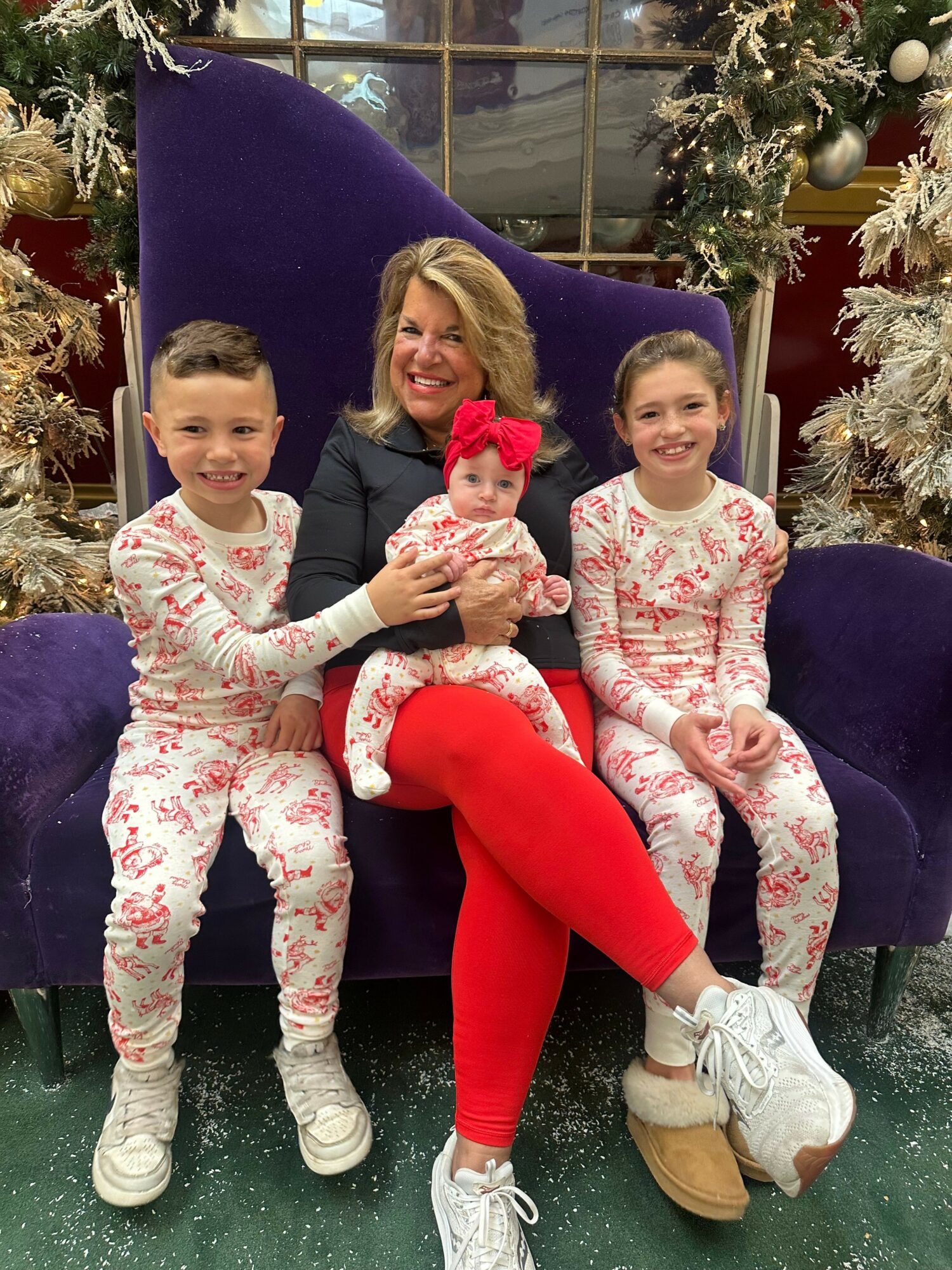 Two children and an adult sitting on a purple chair, all wearing festive clothing, with Christmas decorations in the background.