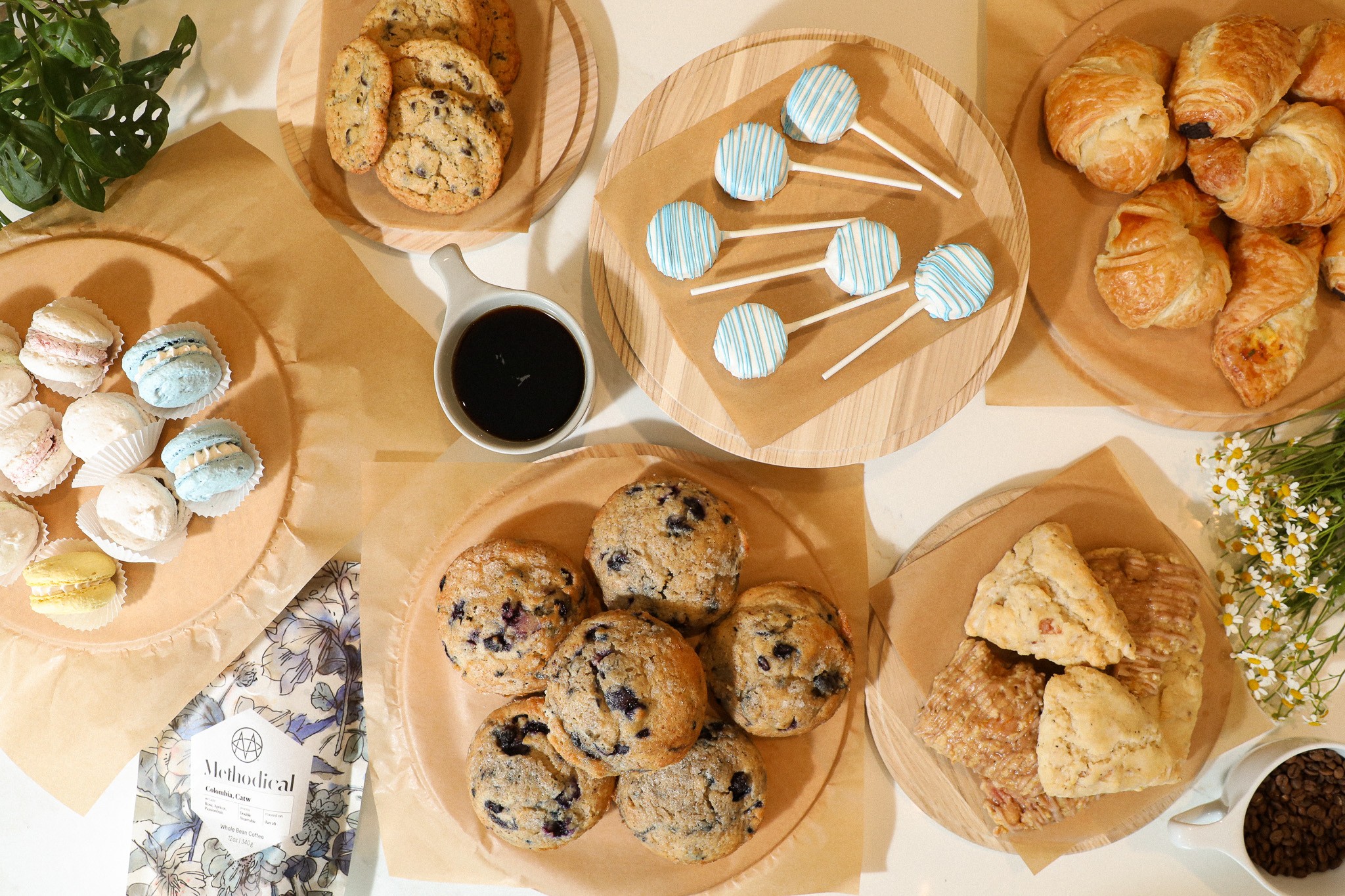 Assorted baked goods and candies on plates with a cup of coffee, including muffins, cookies, cake, and croissants.