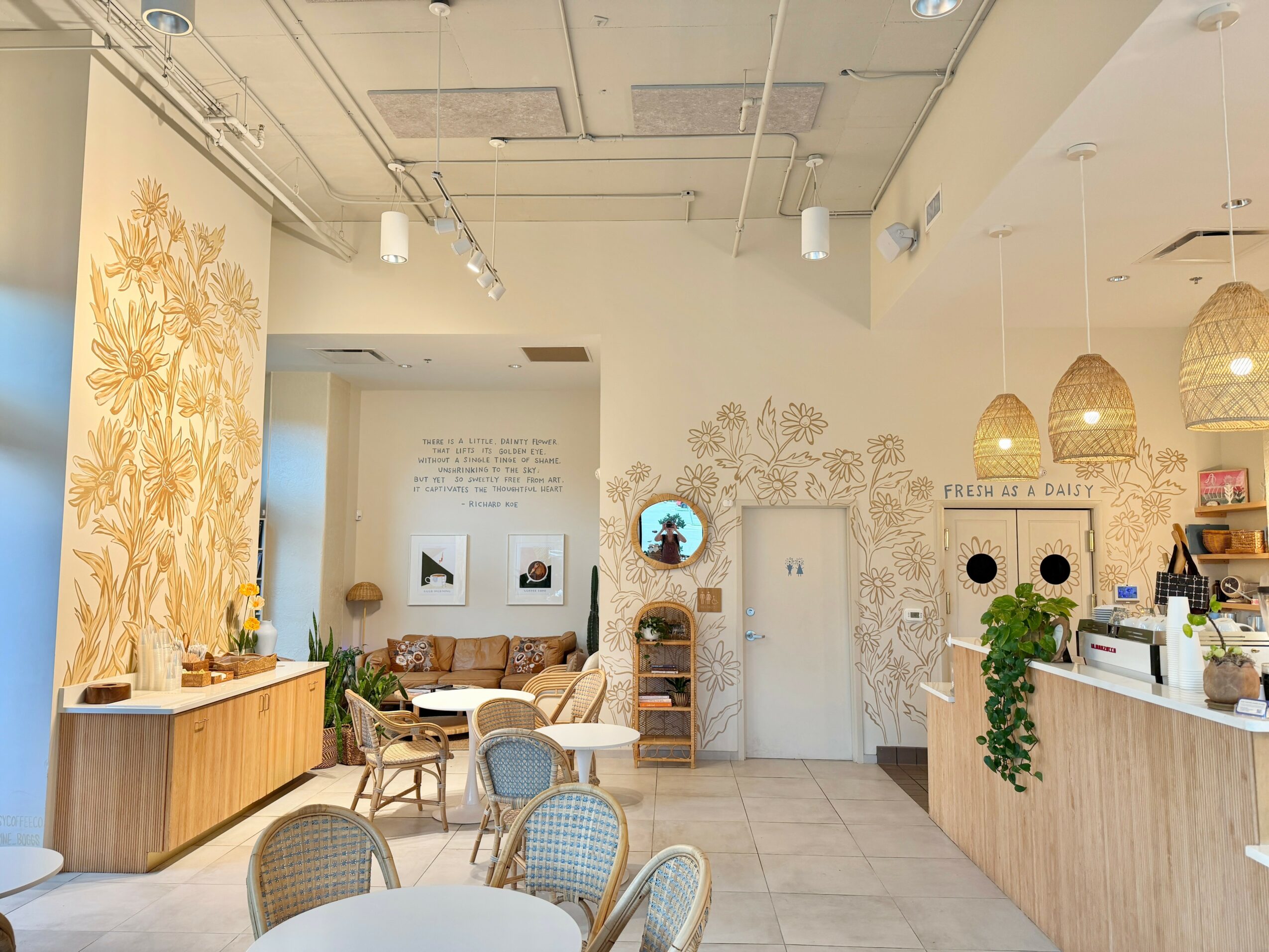 Cafe interior with tables, chairs, wall art, and a counter area with hanging lamps, plants, and decor.
