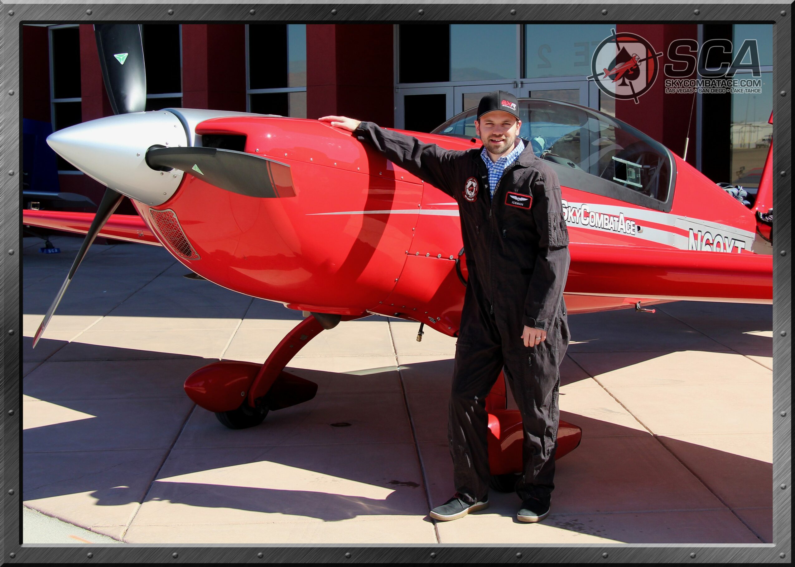 Person standing next to a red and white aircraft on display outdoors, with a building in the background.