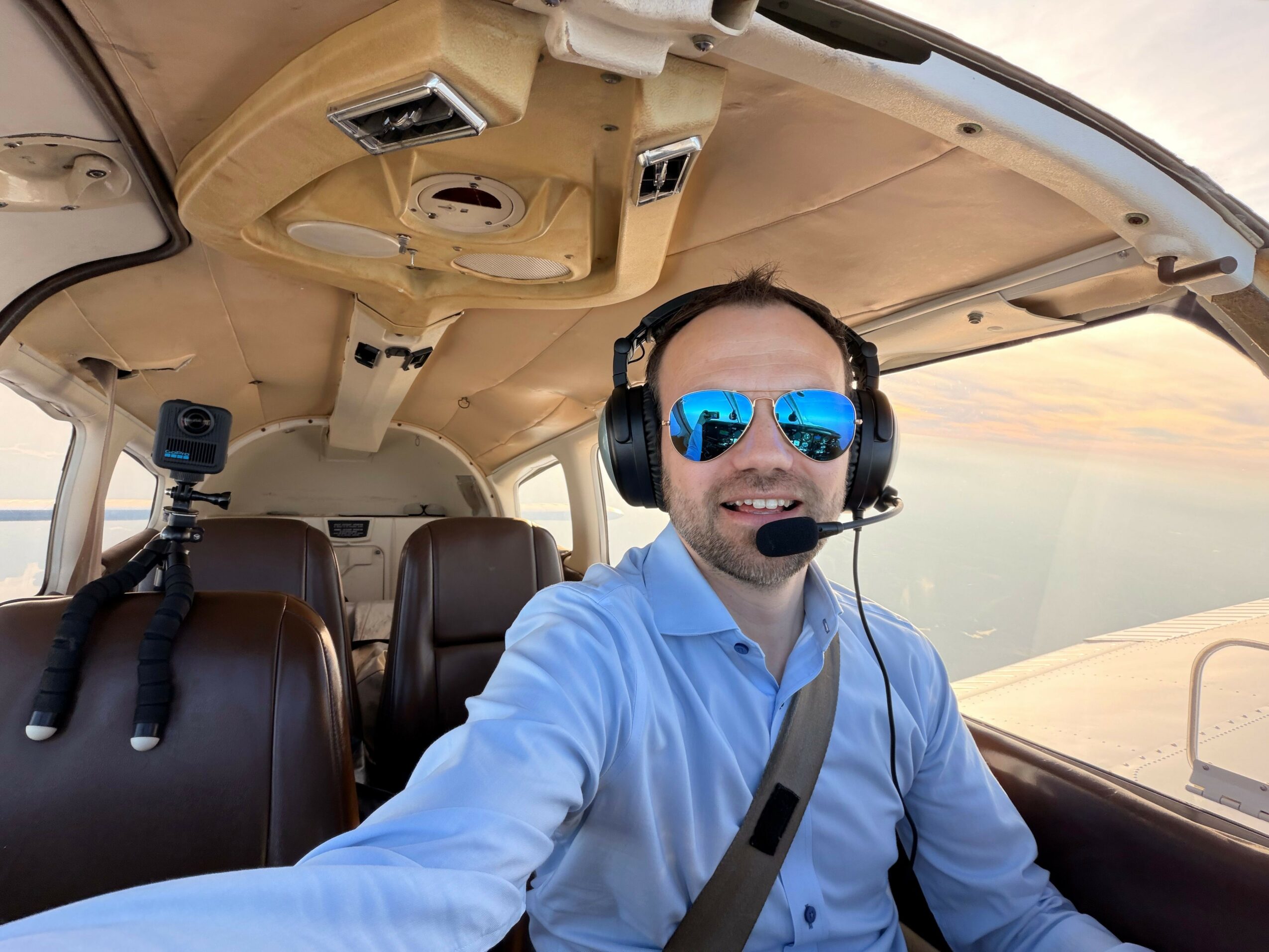 Person wearing sunglasses and headphones taking a selfie inside a helicopter cockpit with beige interior.