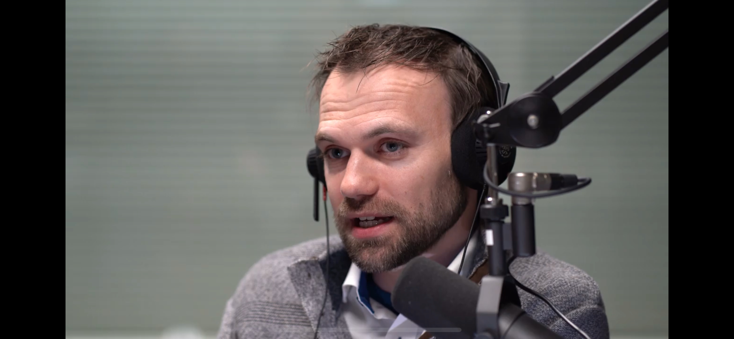 Man with headphones speaking into a microphone in a recording studio.