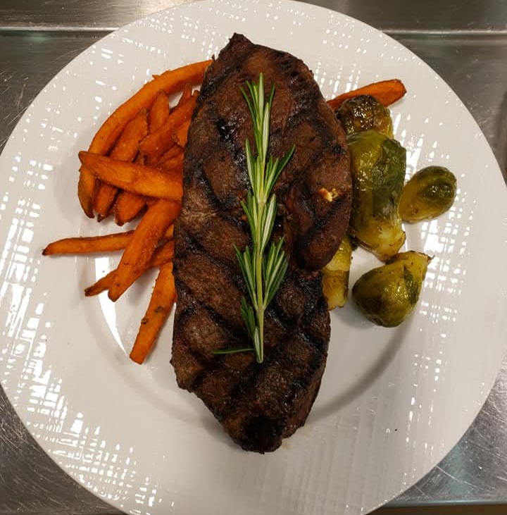 Grilled steak with roasted vegetables and sweet potato fries on a white plate, garnished with a sprig of rosemary.