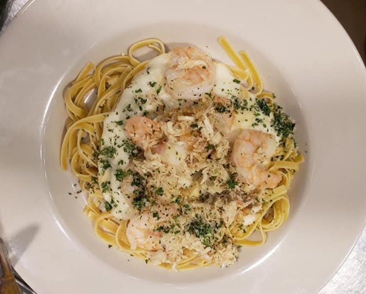 Plate of pasta with shrimp, creamy sauce, herbs, and grated cheese, served on a white dish.