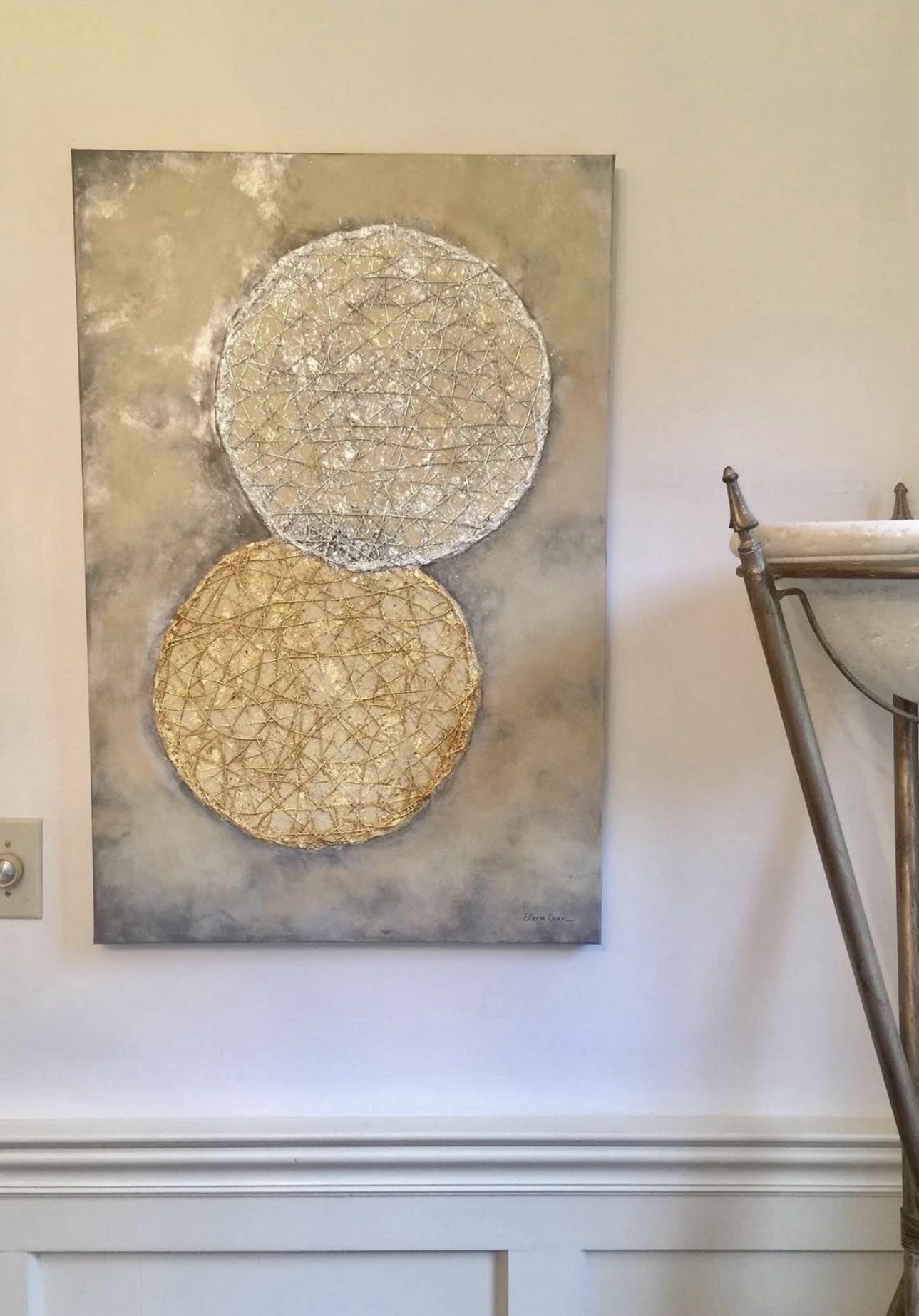 Abstract artwork with two textured circles, one above the other, on a neutral background, hung on a wall.