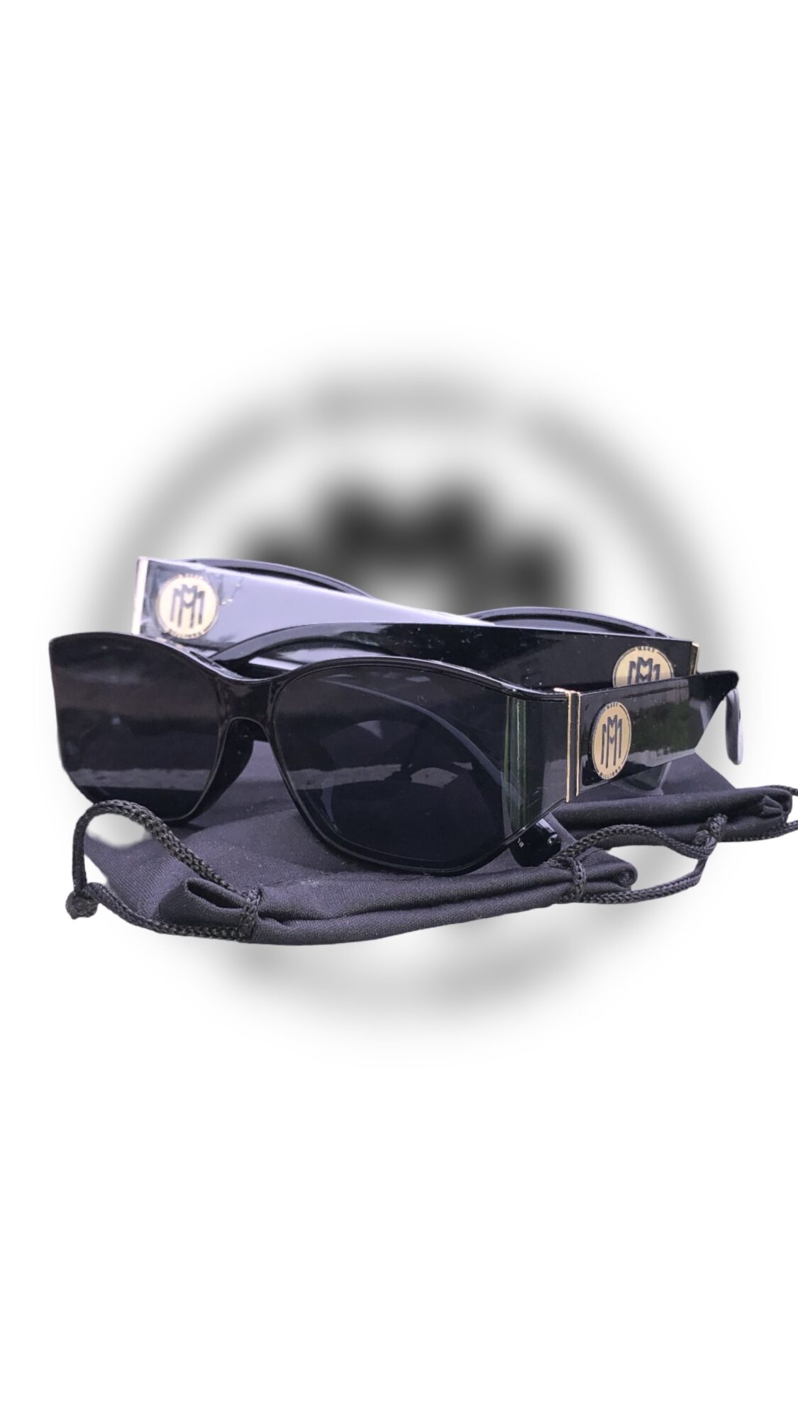 Pair of black sunglasses with a strap, placed on a gray surface, with a blurred background.