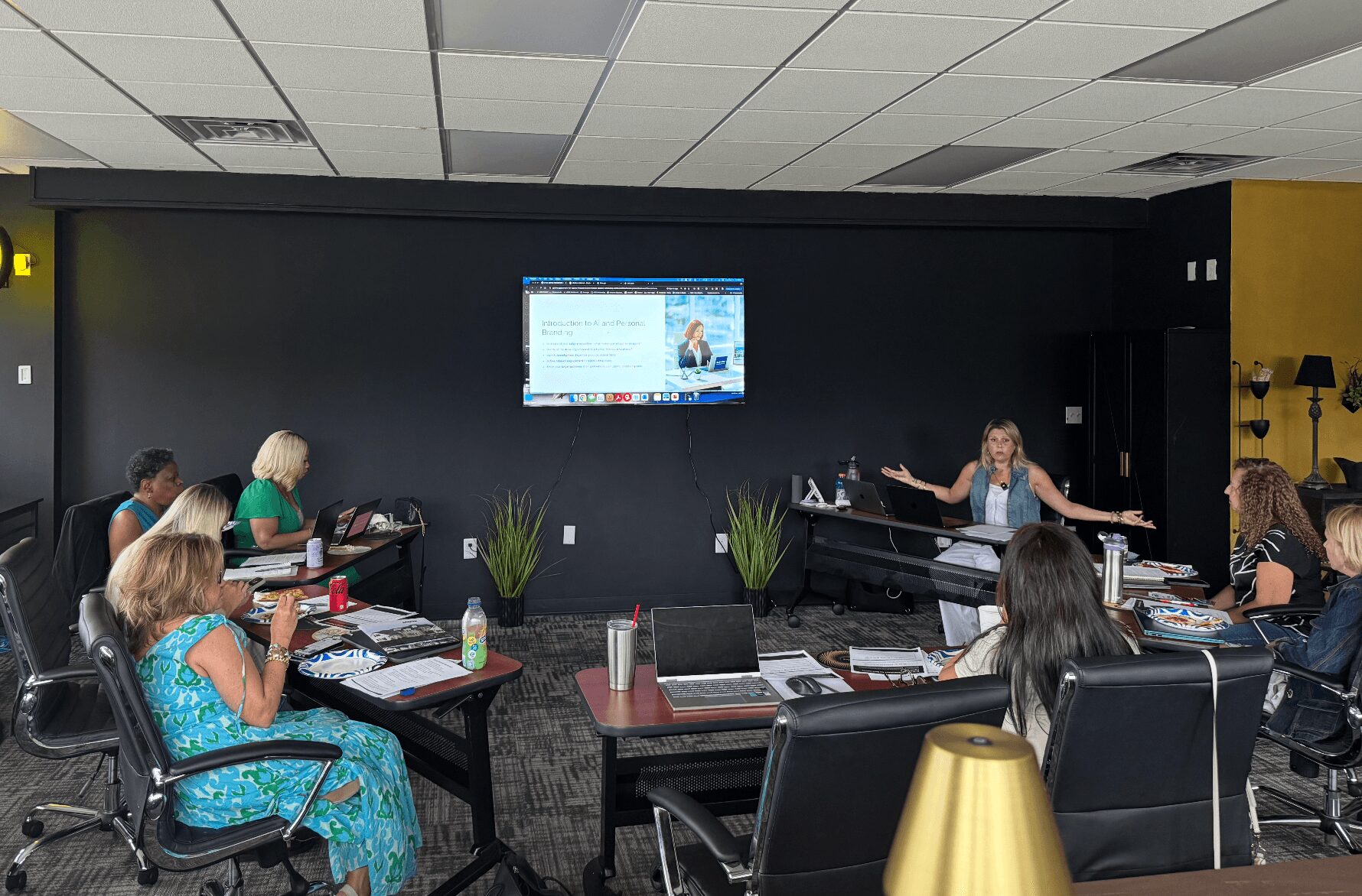 People seated around a conference table in a room with a large screen on the wall, some taking notes.