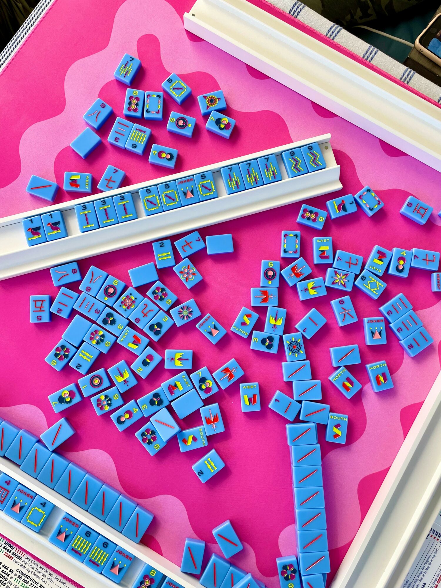 Colorful domino tiles scattered on a pink surface with a white tray holding more dominoes, some arranged in lines.