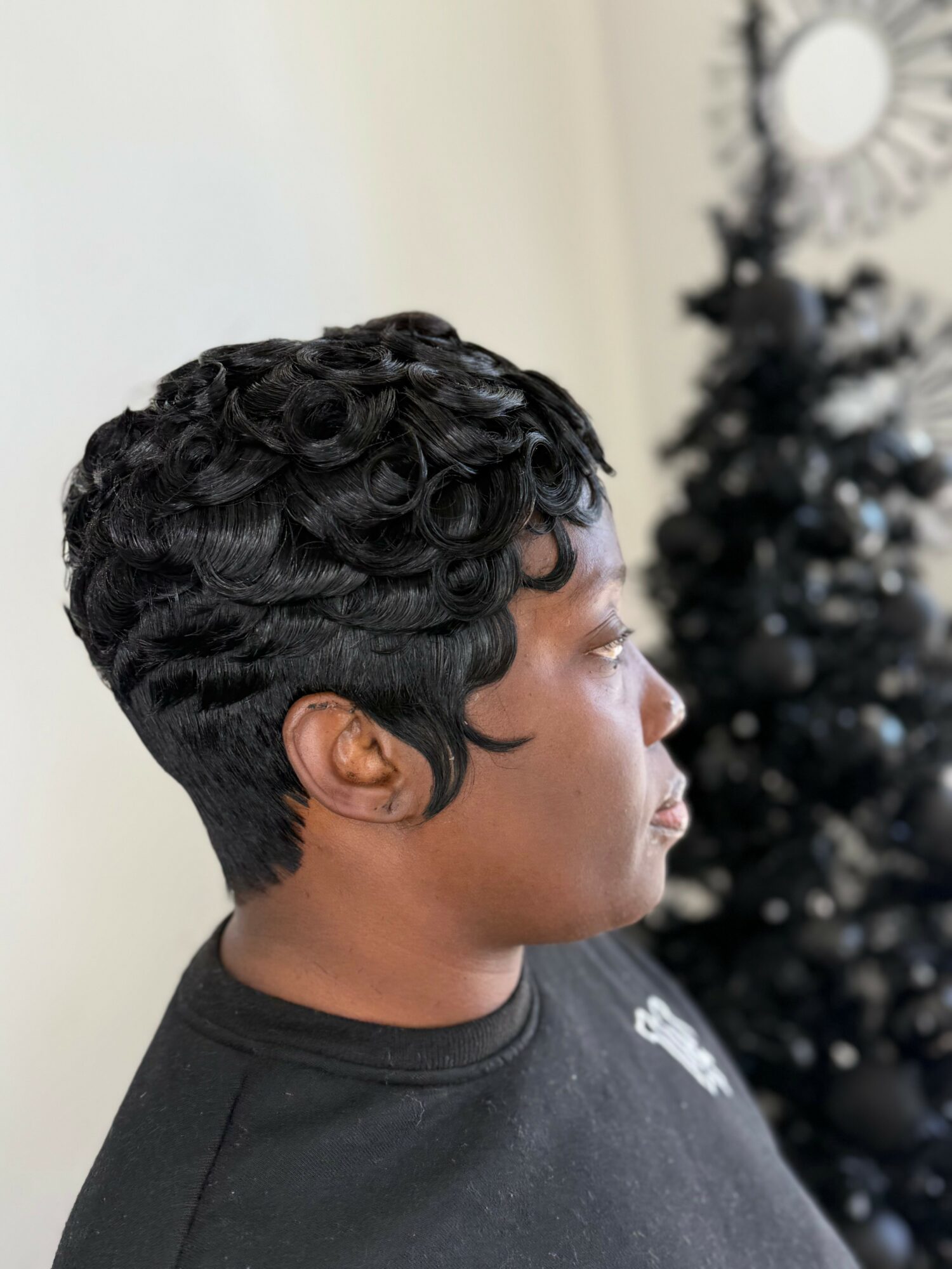 Side profile of a person with short, curly black hair, wearing a black shirt, with a blurred Christmas tree in the background.