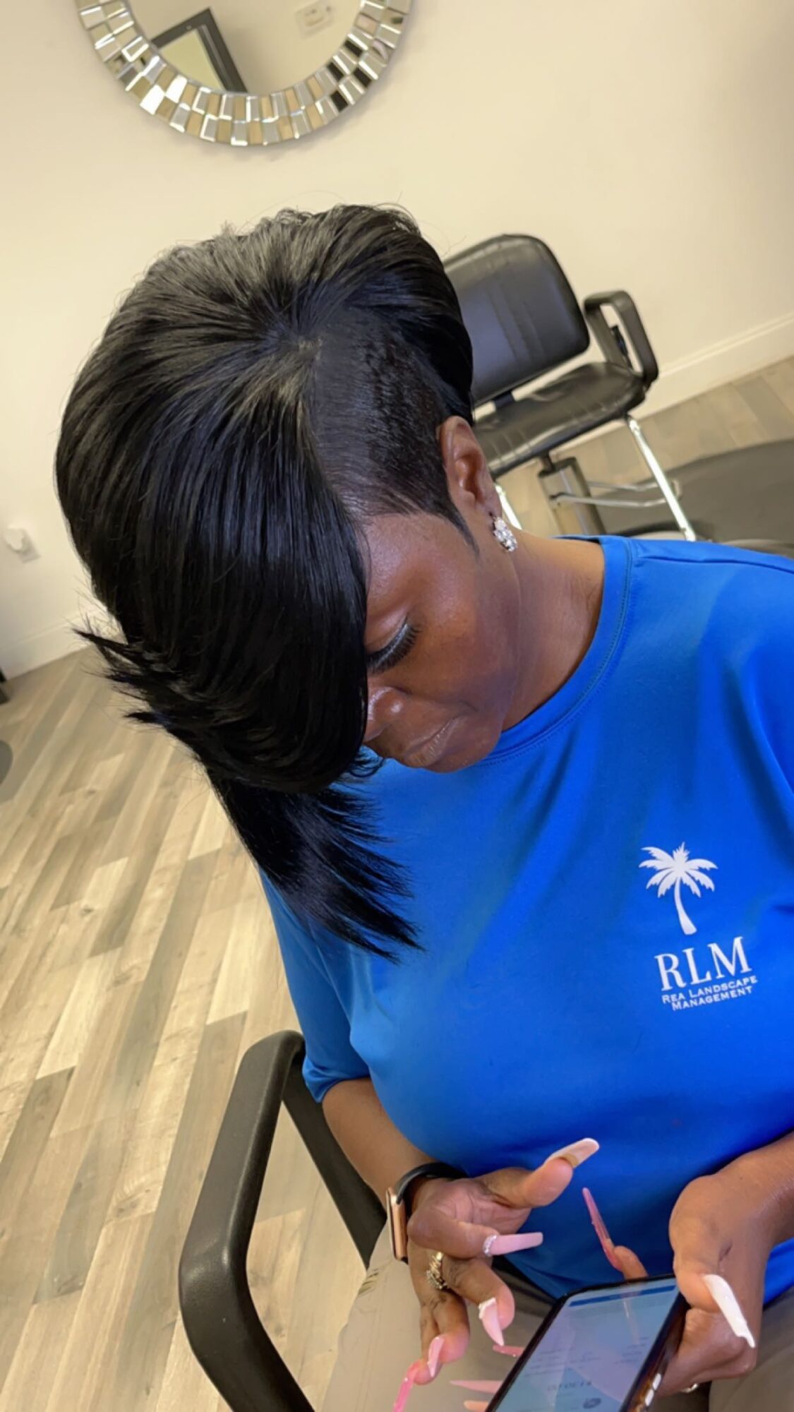 Woman with a short, layered hairstyle looking down at her phone in a salon chair.