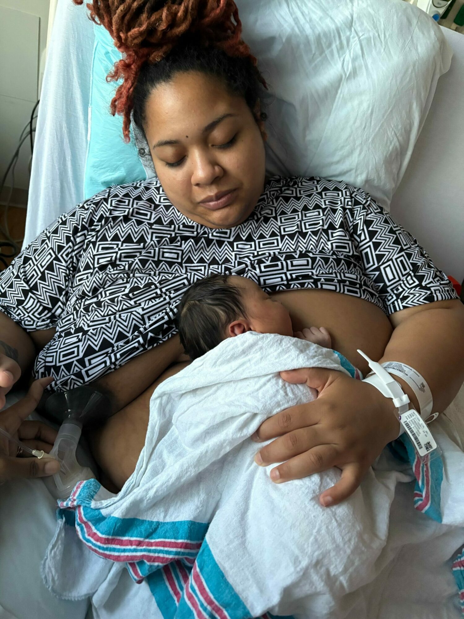 A woman lying in bed holding a child, both resting with eyes closed, in a hospital setting.