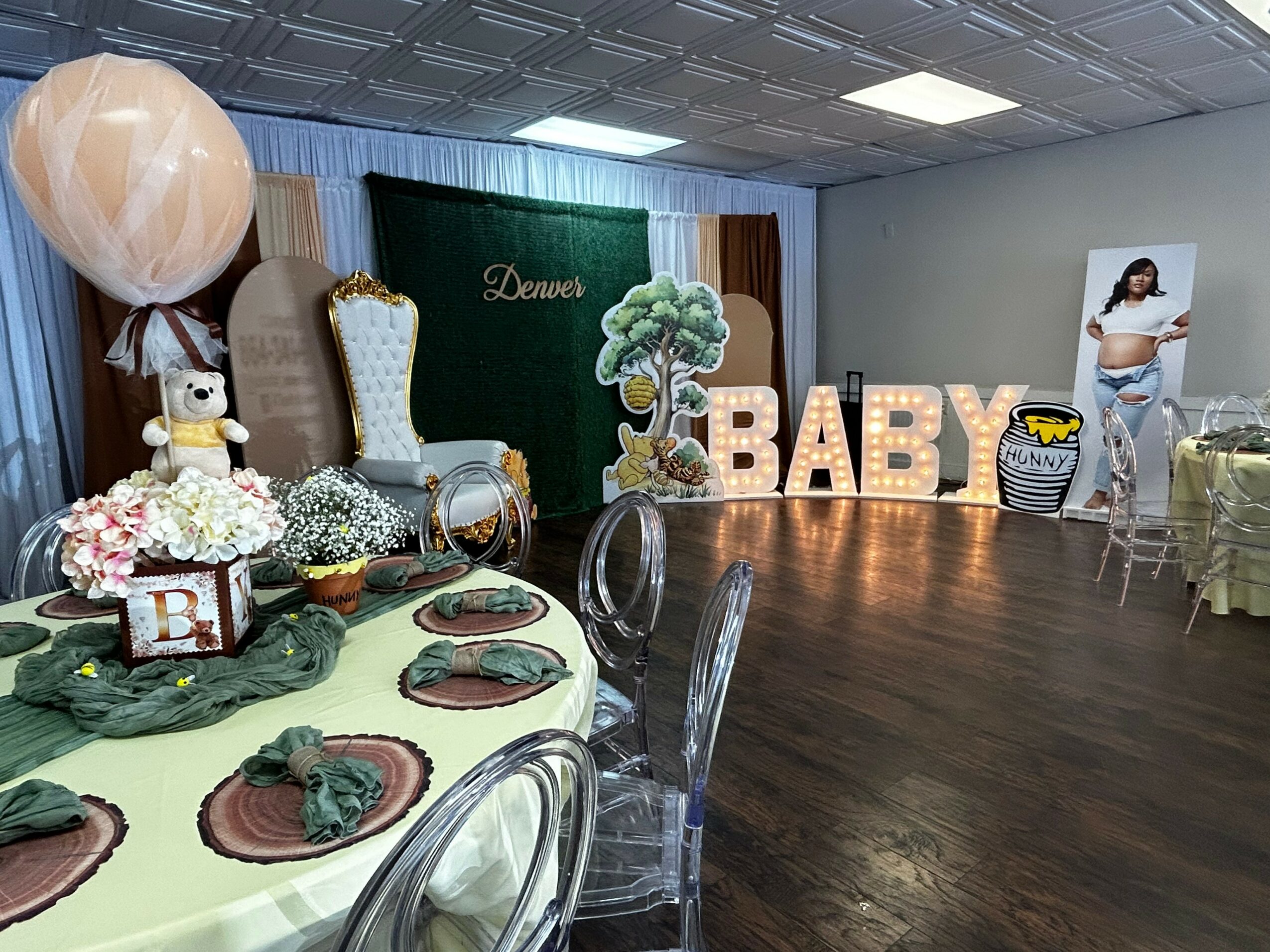 Baby shower setup with decorated table, large illuminated letters spelling BABY, and a woman standing nearby, in a decorated room.