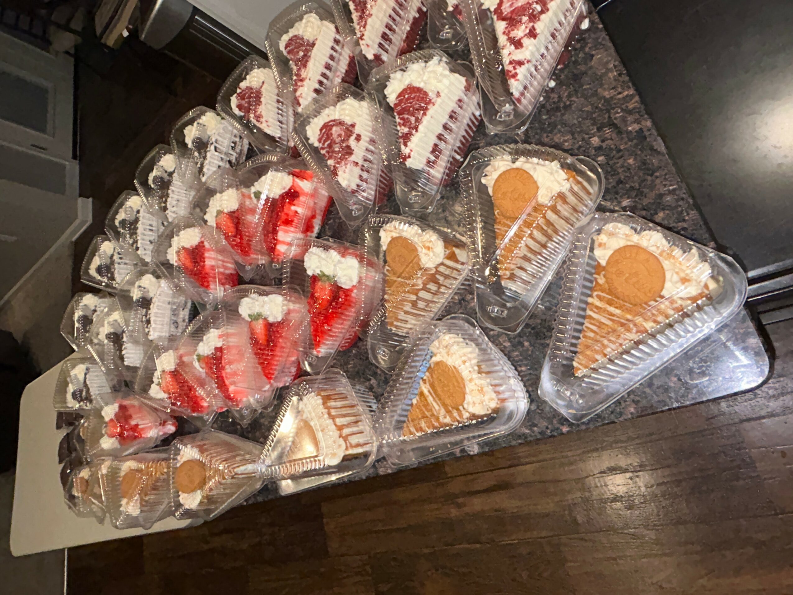 Assorted desserts including slices of cake, cupcakes, and cookies arranged on a dark countertop.