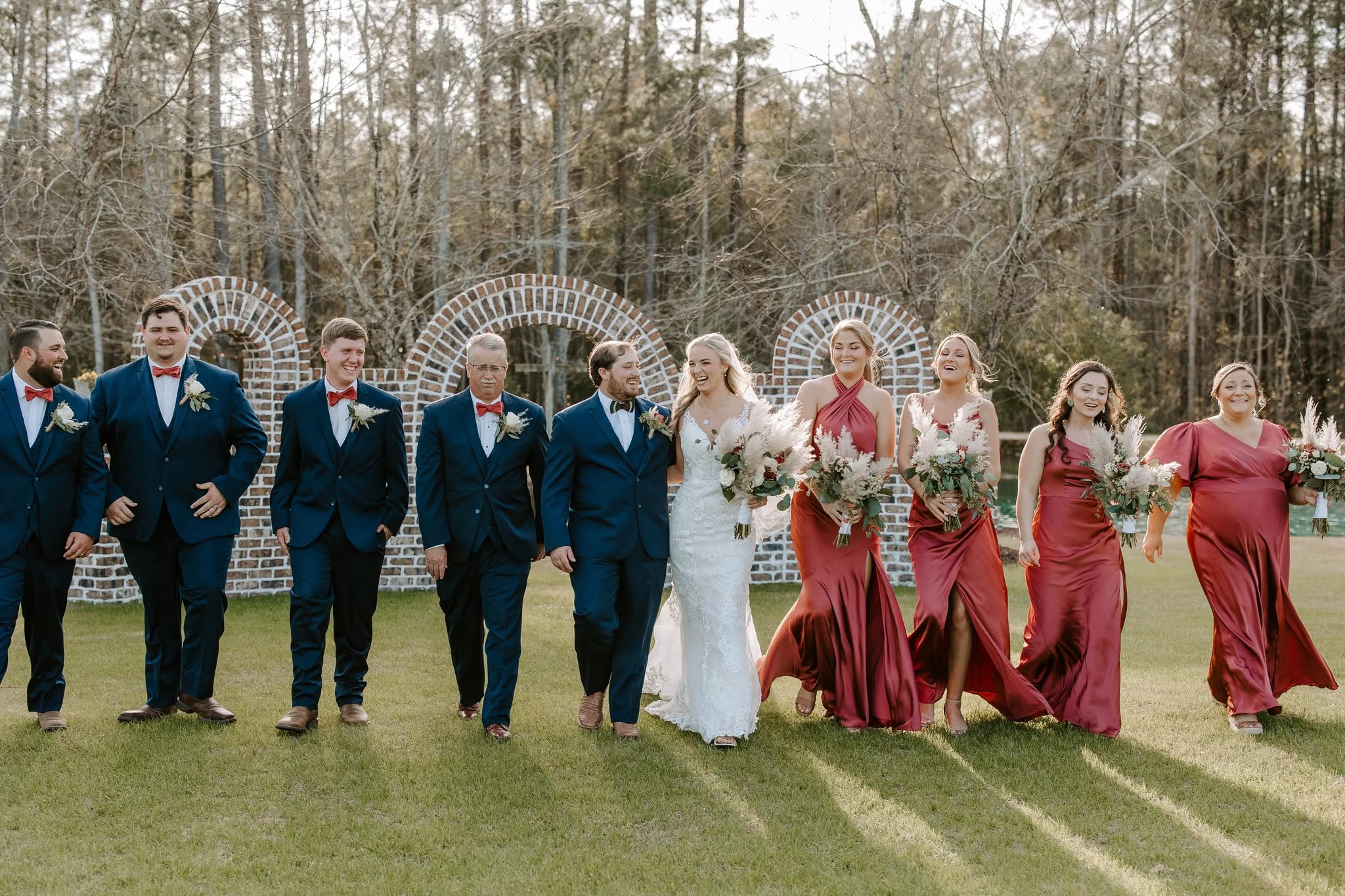 Group of people in formal attire standing outdoors on grass, with trees in background, during a wedding celebration.