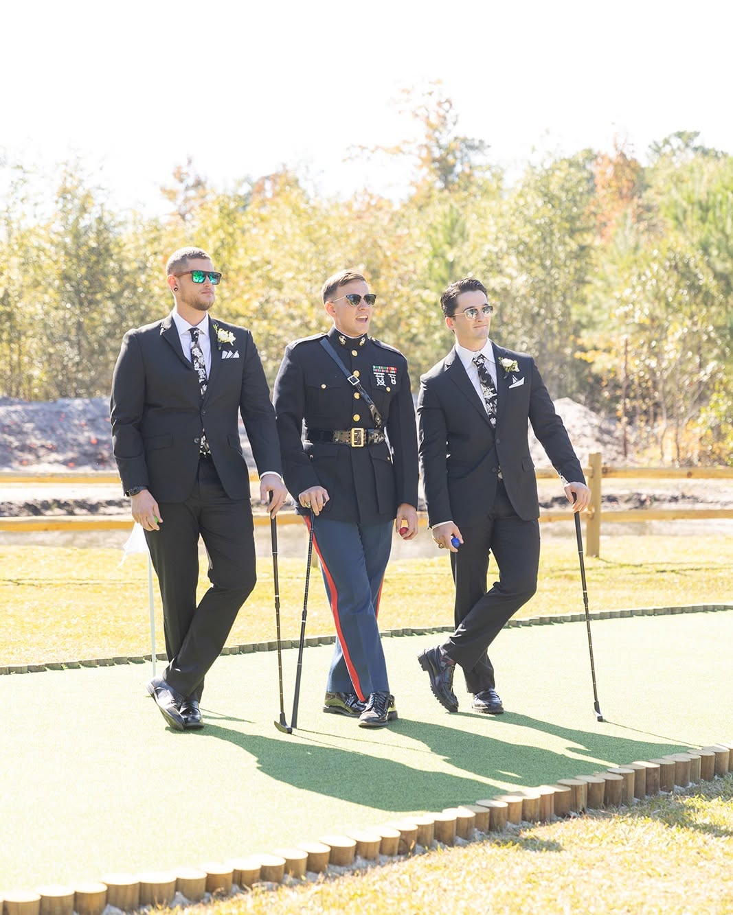 Three men in military uniforms walking on a golf course with trees in the background, holding golf clubs.