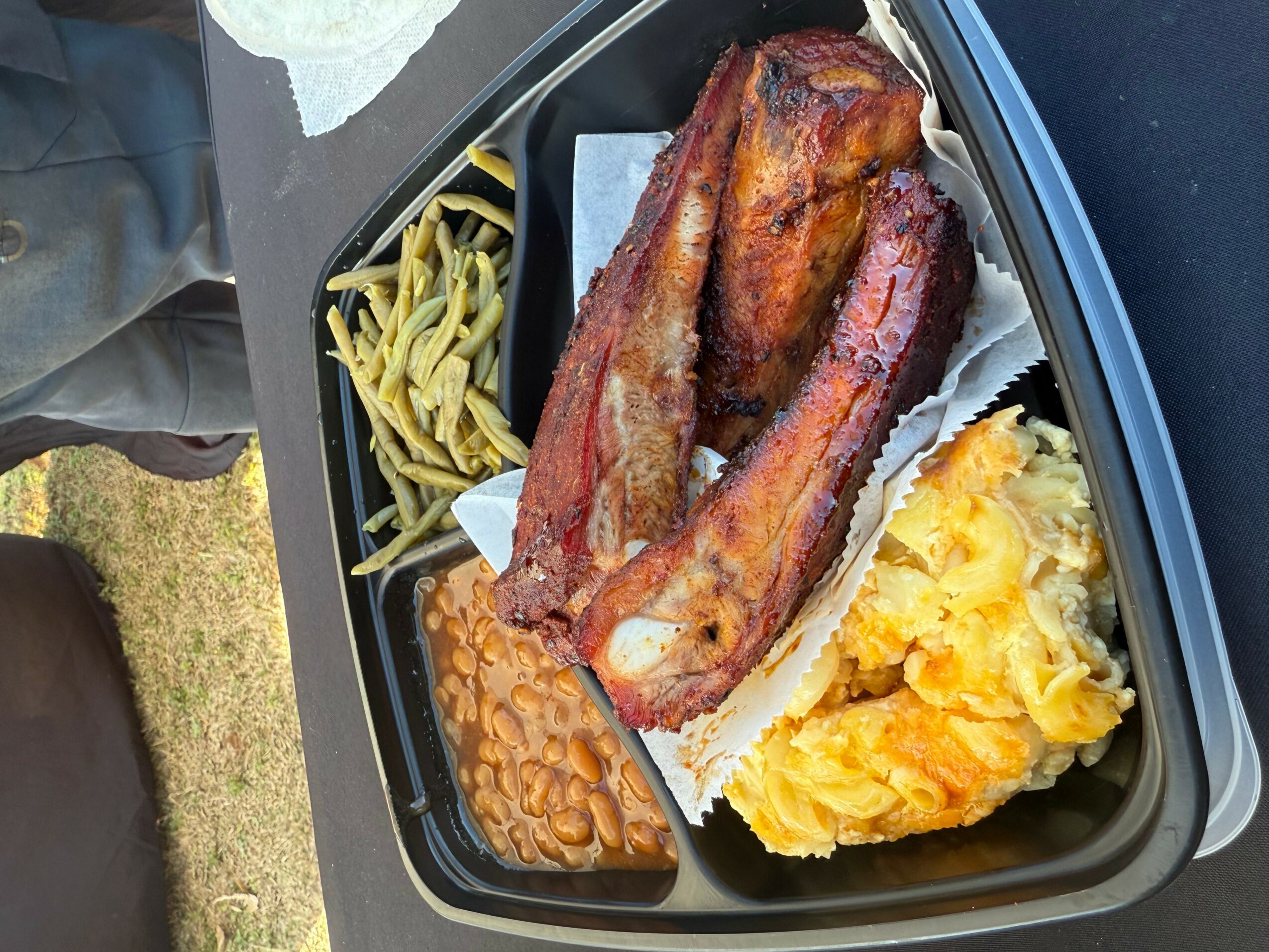 Barbecue ribs, baked beans, macaroni and cheese, and green beans on a black tray.