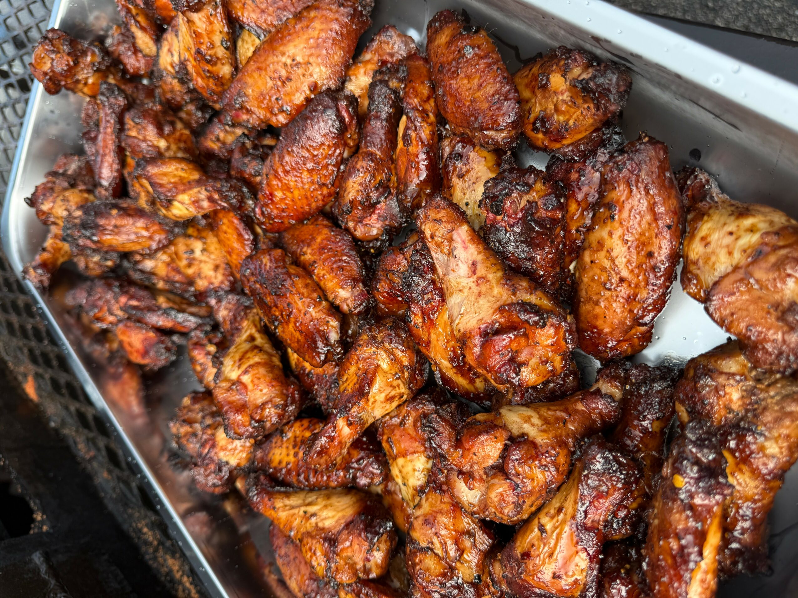 Tray of cooked, crispy chicken drumsticks and wings with a dark, glazed appearance.