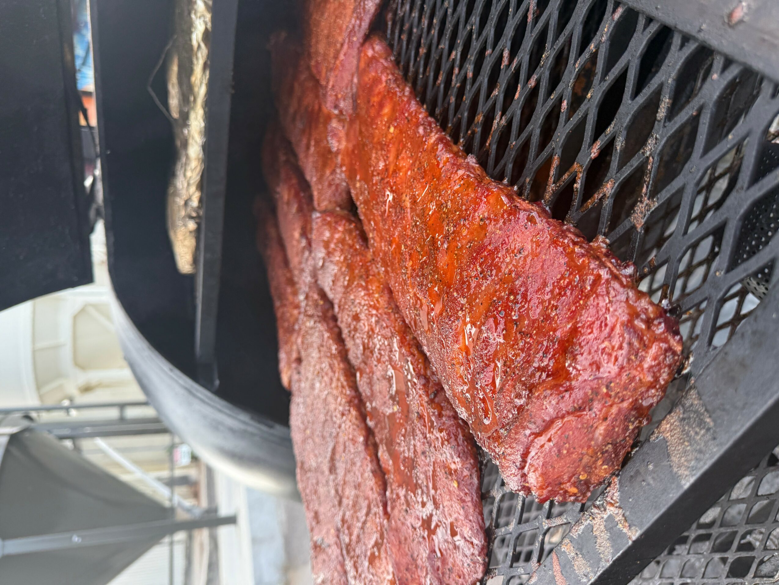 Two cooked ribs on a black grill rack, with a reddish-brown glaze, placed on a grill surface.