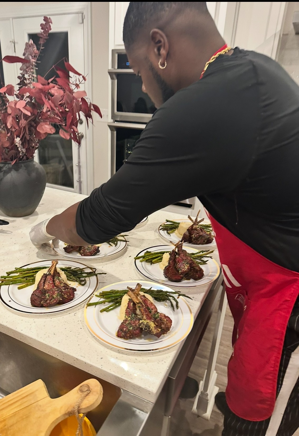 Person preparing plates of cooked meat garnished with herbs on a kitchen counter, with a potted plant in the background.