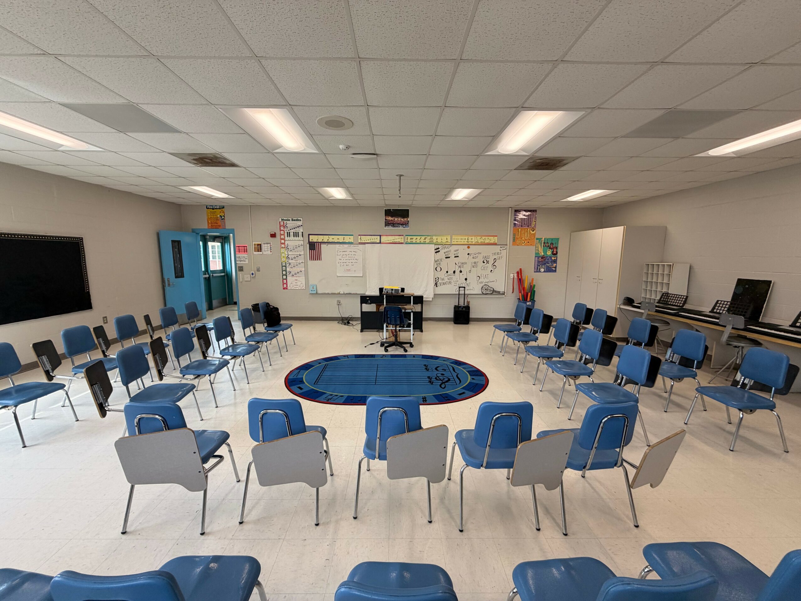 Classroom with chairs arranged in a circle around a blue rug, white walls, and a whiteboard at the front.