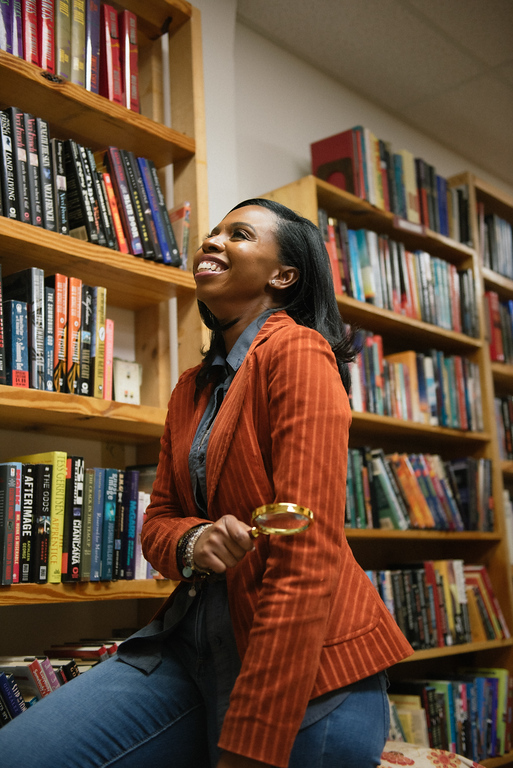 Woman smiling and looking up in a library with bookshelves behind her.