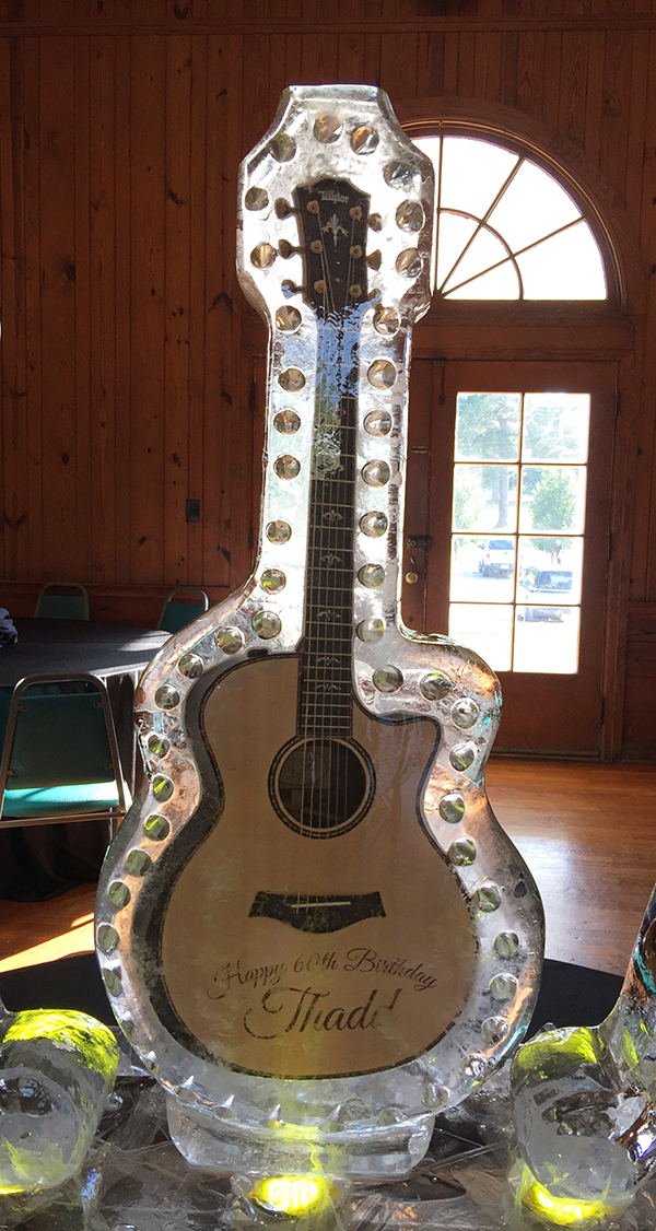 Ice sculpture shaped like a guitar with a window in the background, inside a wooden room.