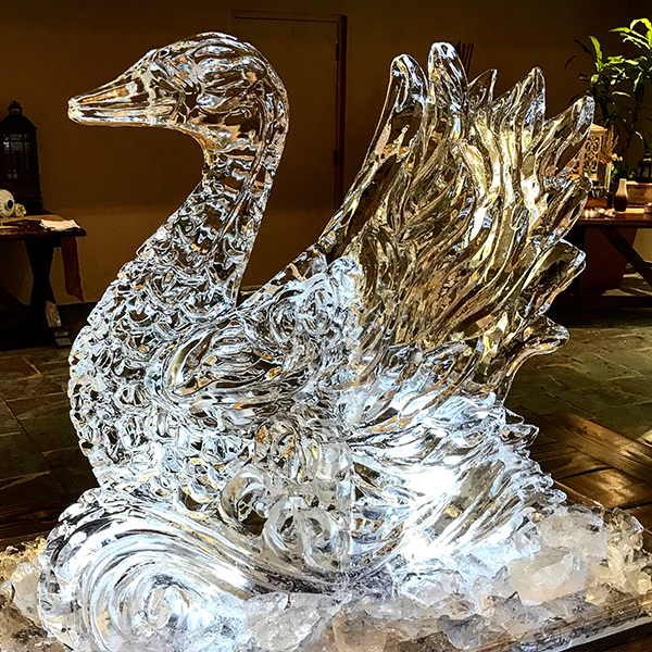 Intricately carved glass swan sculpture with detailed feathers and a curved neck, displayed indoors on a wooden surface.