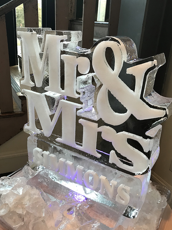 Ice sculpture with the words 'Mr & Mrs' and 'LOVE' illuminated, set on ice blocks, in a room with windows and chairs