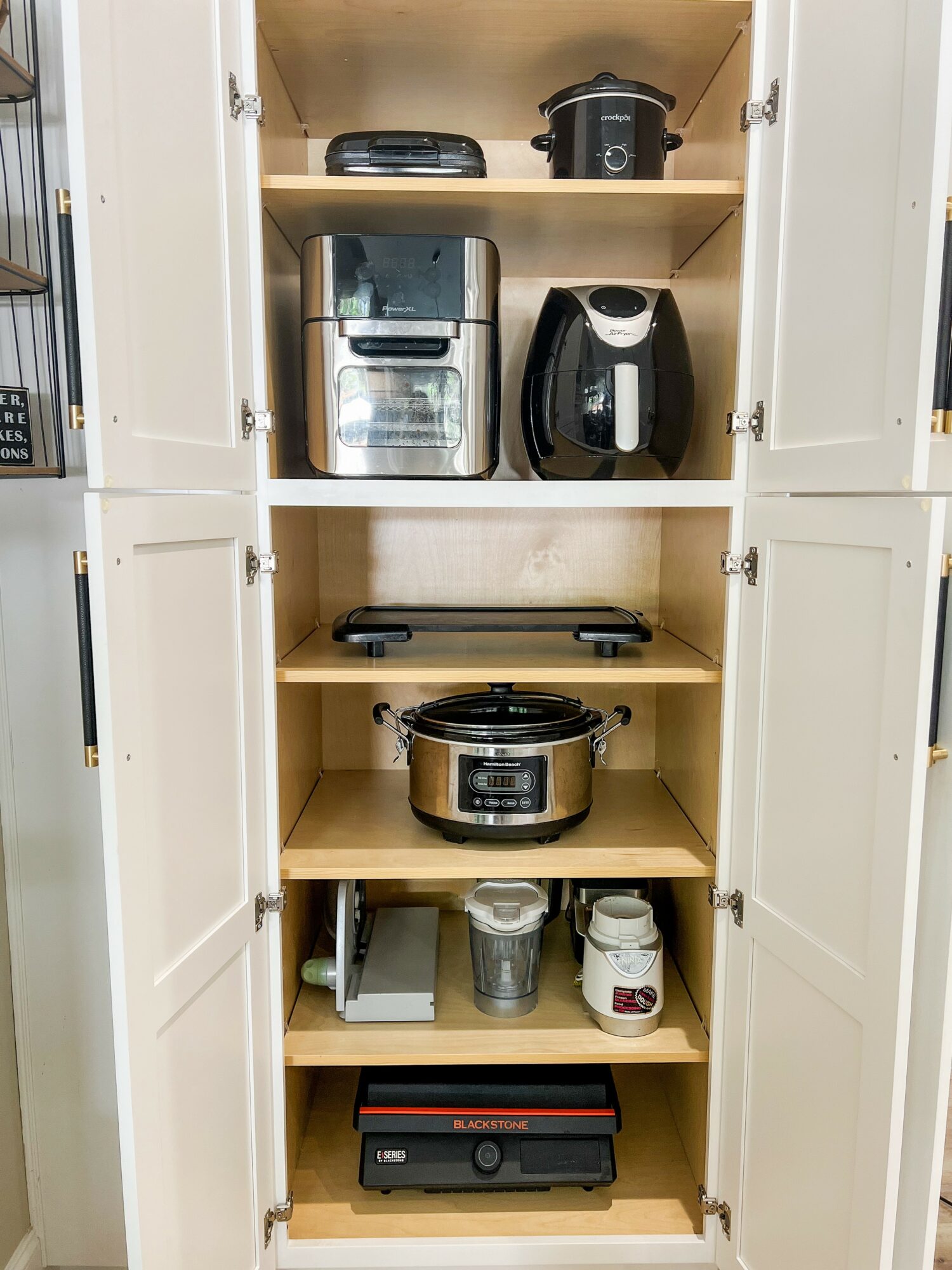 Kitchen cabinet with appliances including a rice cooker, air fryer, slow cooker, and a black electronic device on shelves.
