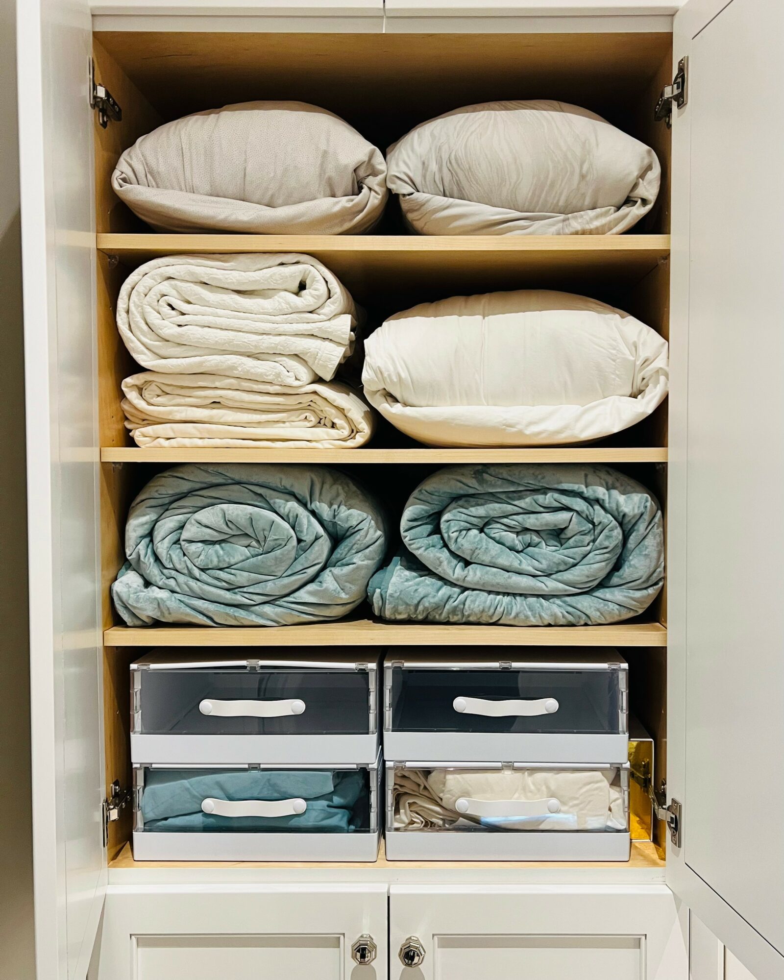 Open cabinet with pillows, blankets, and storage boxes on shelves, organized neatly inside.