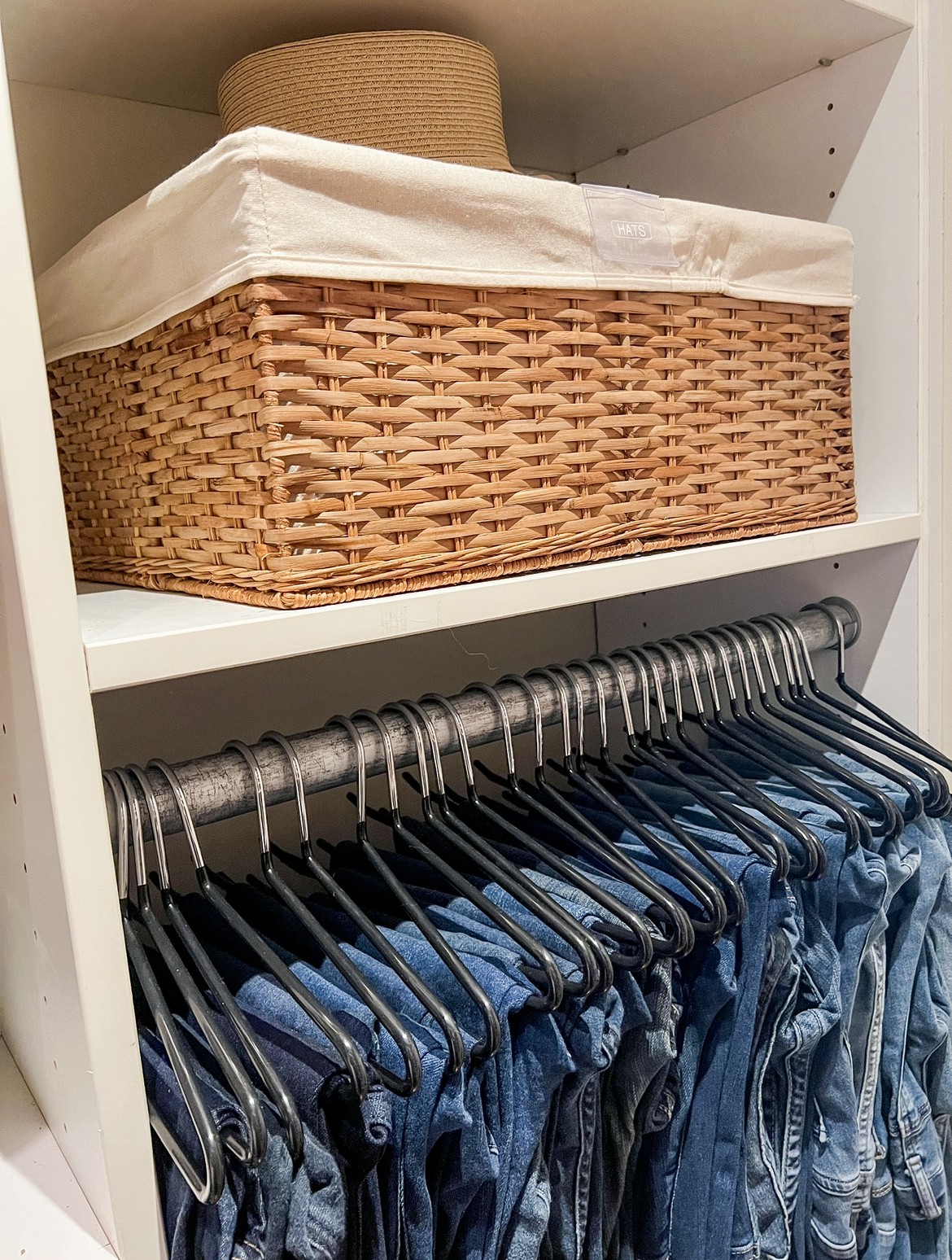 Wicker basket on a shelf above hanging blue jeans in a closet, with a white cloth lining the basket.
