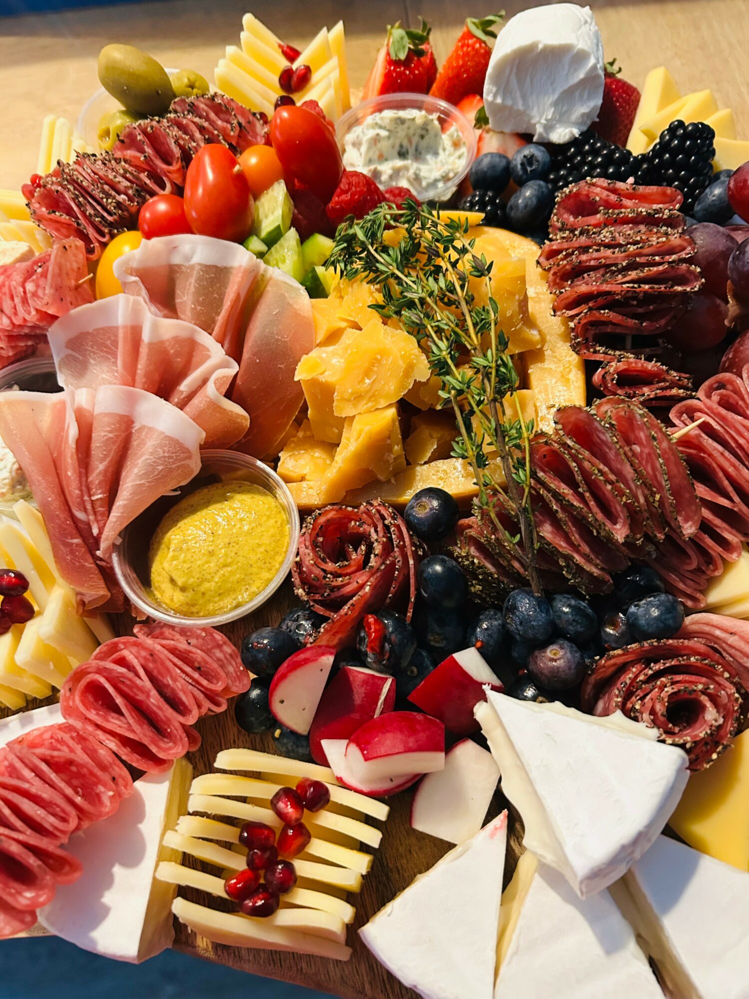 Assorted cheeses, meats, fruits, and garnishes arranged on a platter, including strawberries, blueberries, blackberries, and sliced cured meats.
