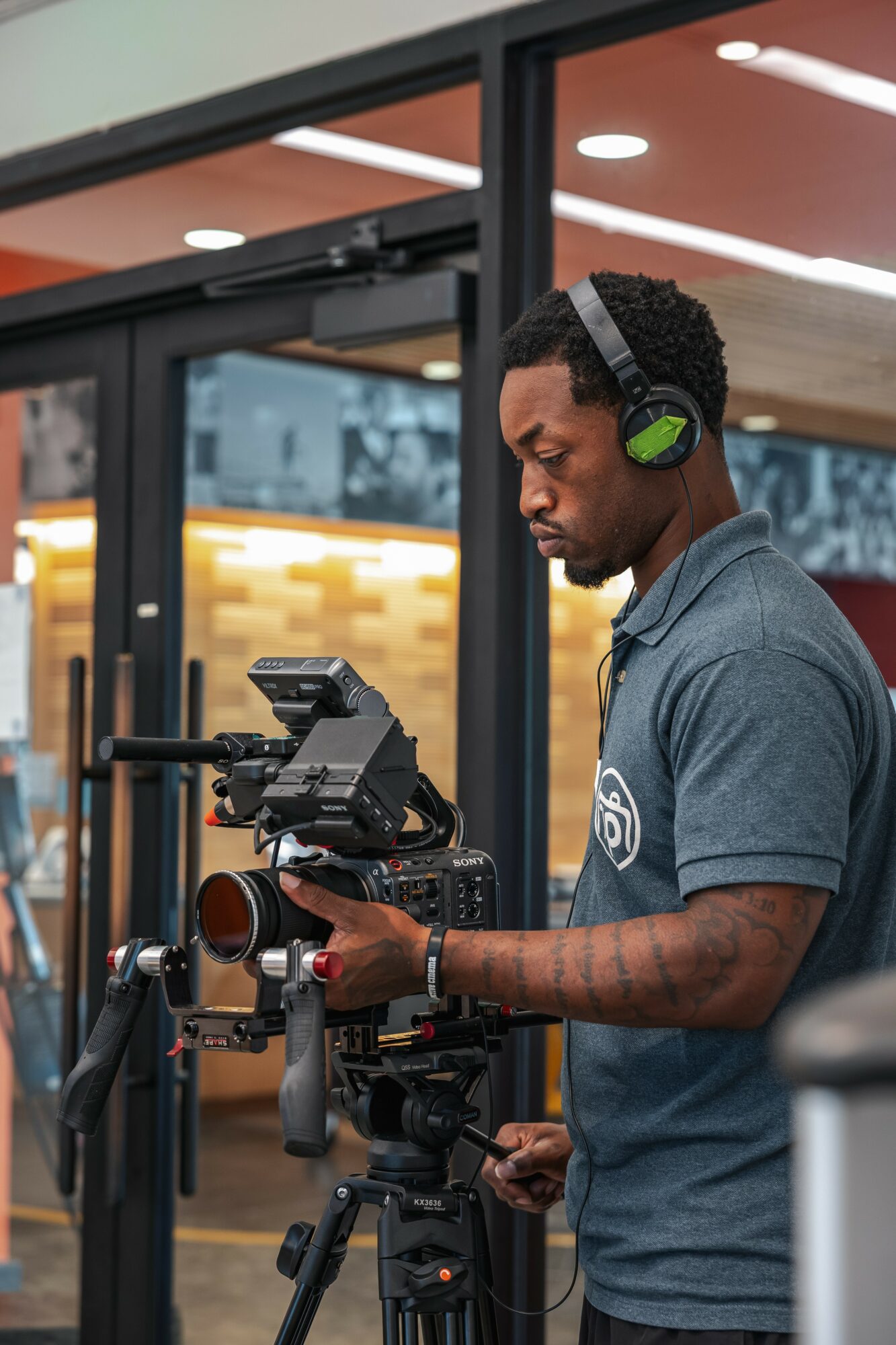 Young man with headphones operating professional video camera indoors, background shows modern interior with warm lighting.