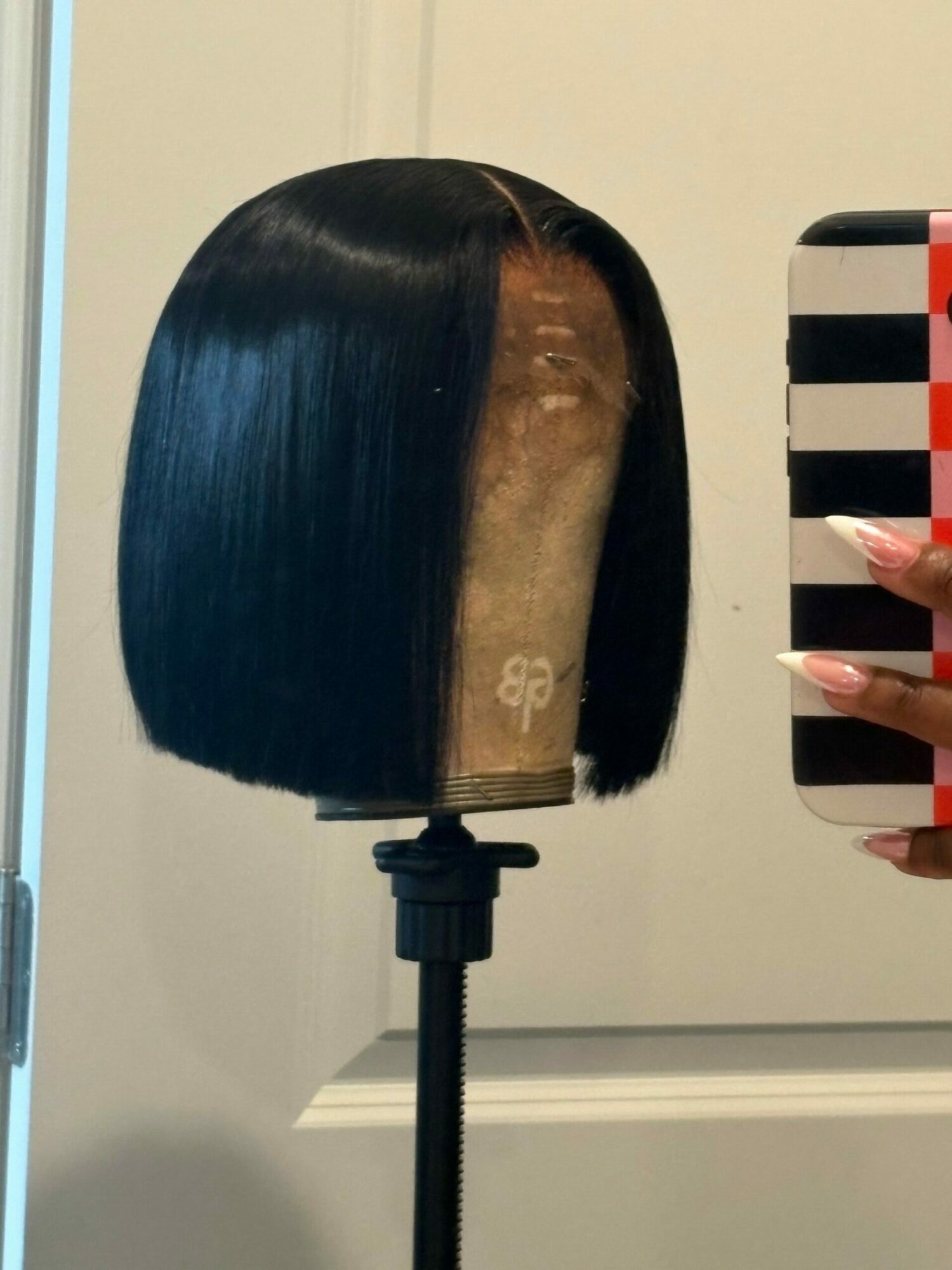 Person holding a mirror showing a hairbrush with black hair and a person's hand with long nails, against a white background.
