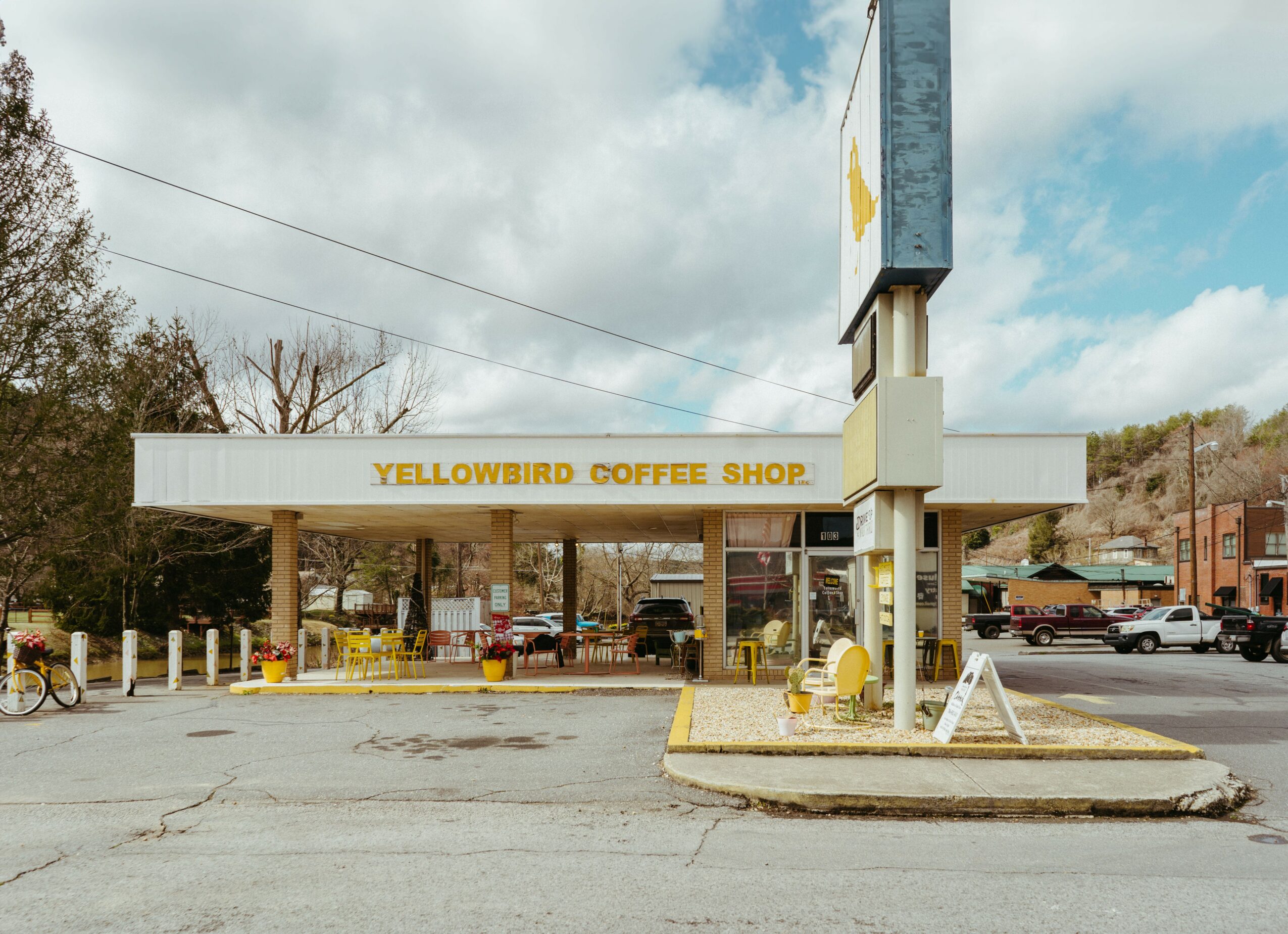 Front view of Yellowbird Coffee Shop with a white facade and yellow signage, under a partly cloudy sky.