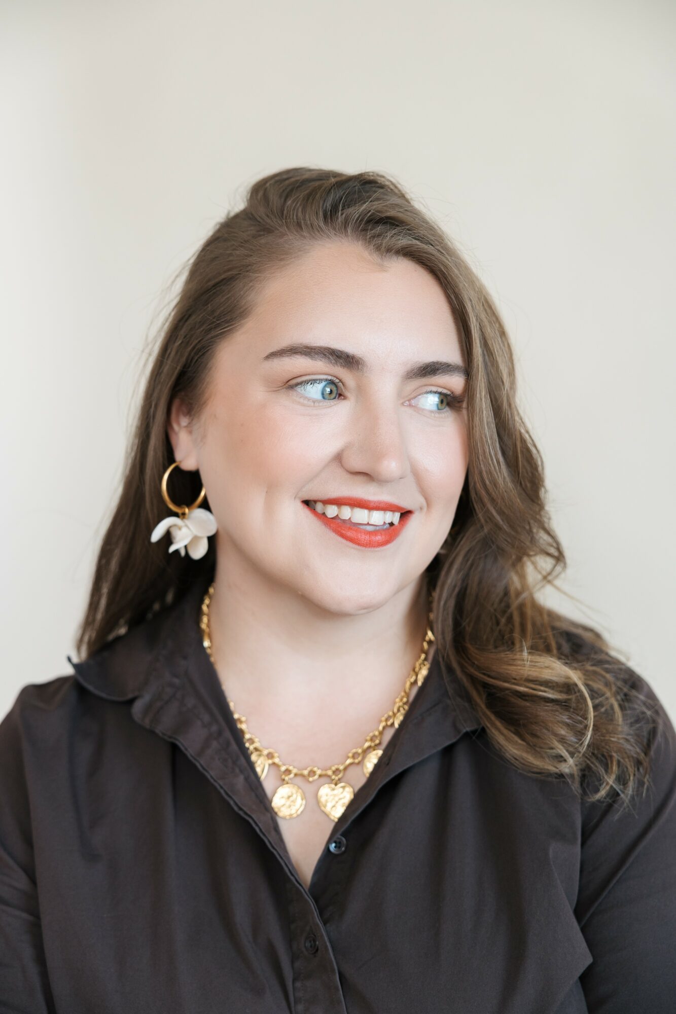 Young woman with wavy hair, wearing earrings and a black shirt, smiling and looking to the side.