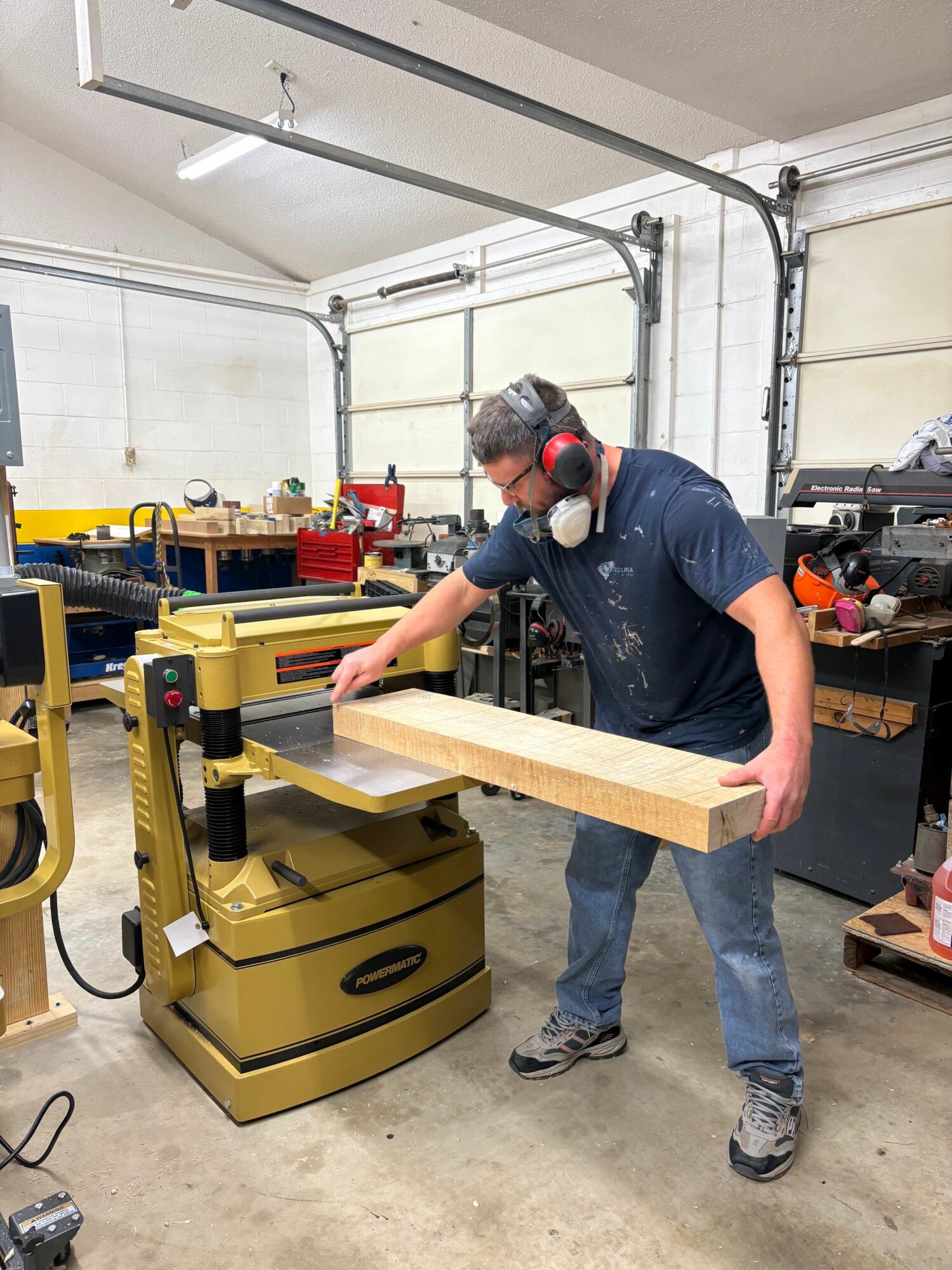 Person wearing safety glasses and ear protection using a machine to cut a wooden board in a workshop.