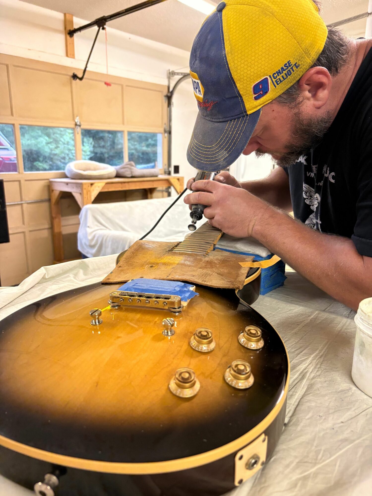 Person working on a yellow and black guitar, adjusting or repairing it, in a room with wooden walls and a window.