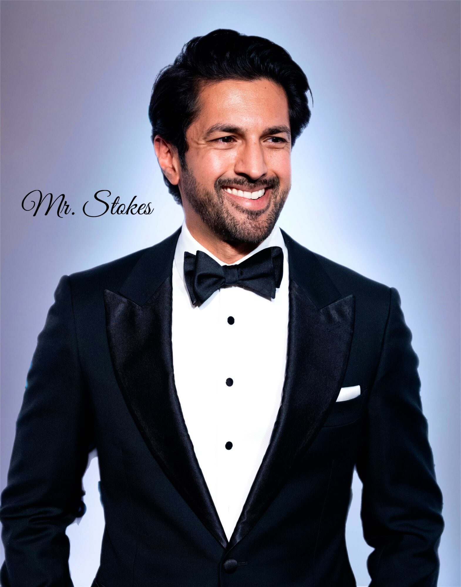 Man in tuxedo with bow tie smiling, background light gradient, text 'Mr. Stokes' on left side.