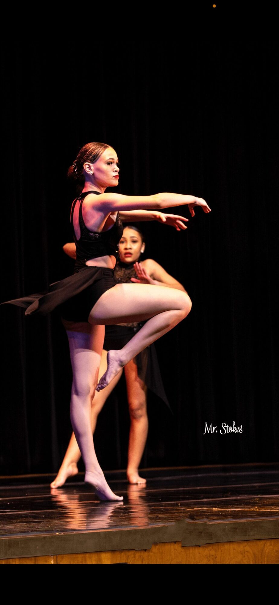 Two ballet dancers perform on stage, one balancing on one leg with arms extended, the other standing behind. Word: Miss Sabel.